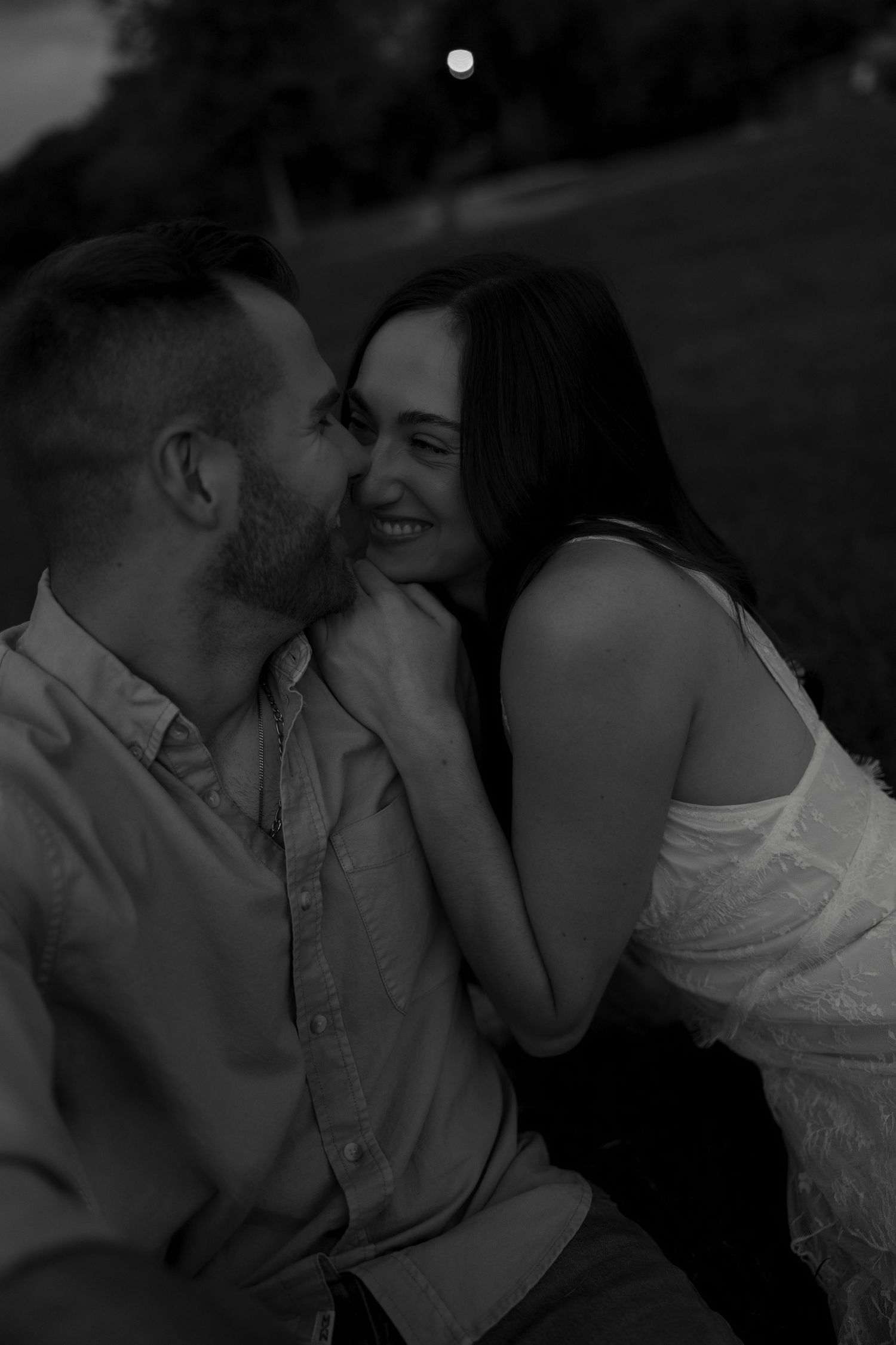 Black and white photo of couple sharing tender cheek kiss during golden hour session.