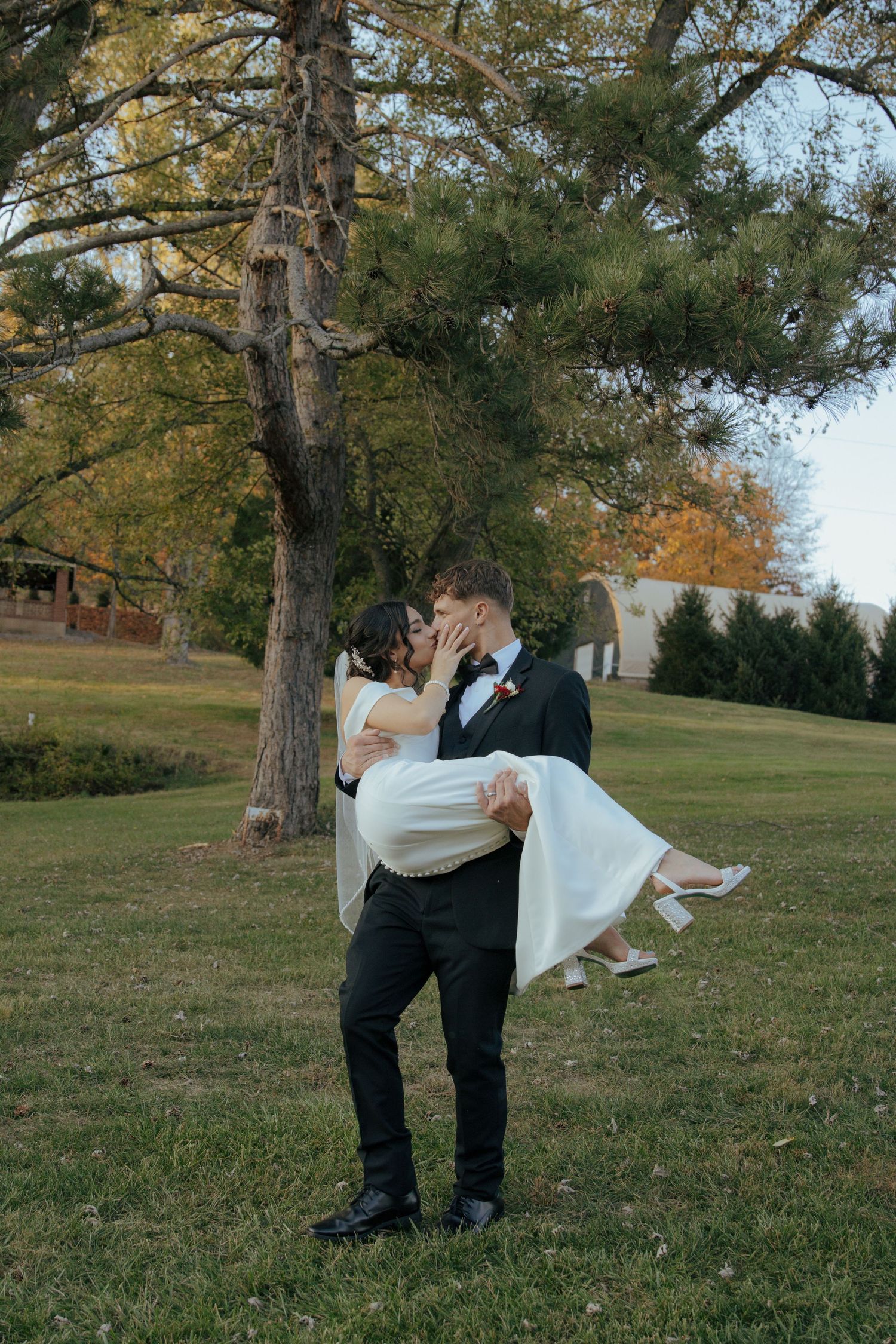 Wedding couple shares romantic moments under tall pine trees in an autumn setting.