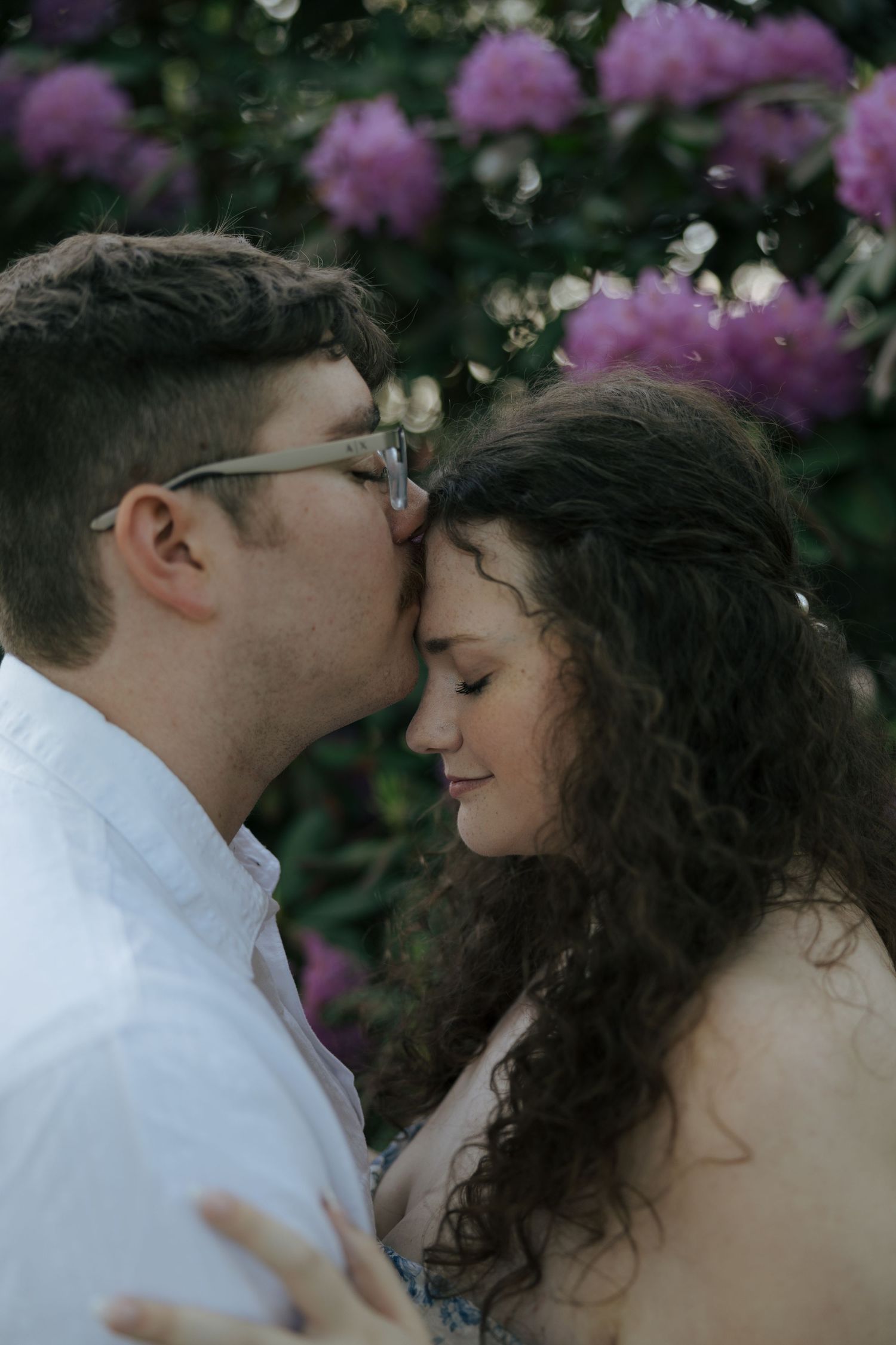 Couple sharing an intimate moment with foreheads together surrounded by blooming pink flowers.
