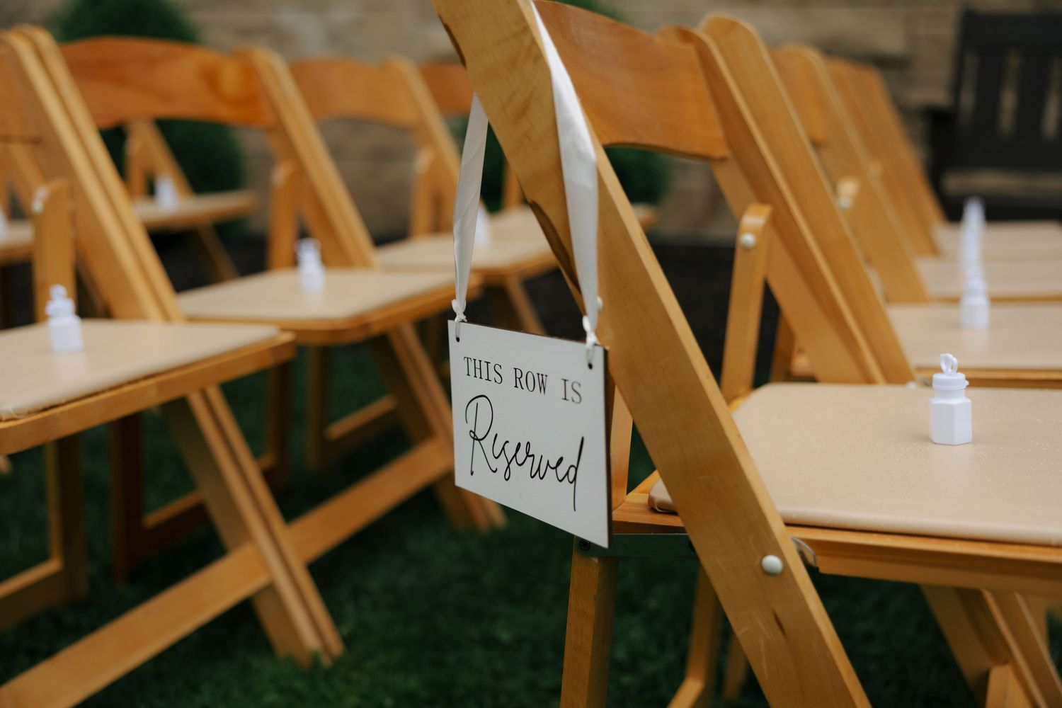 Wooden folding chairs with a reserved row sign at an outdoor wedding ceremony.
