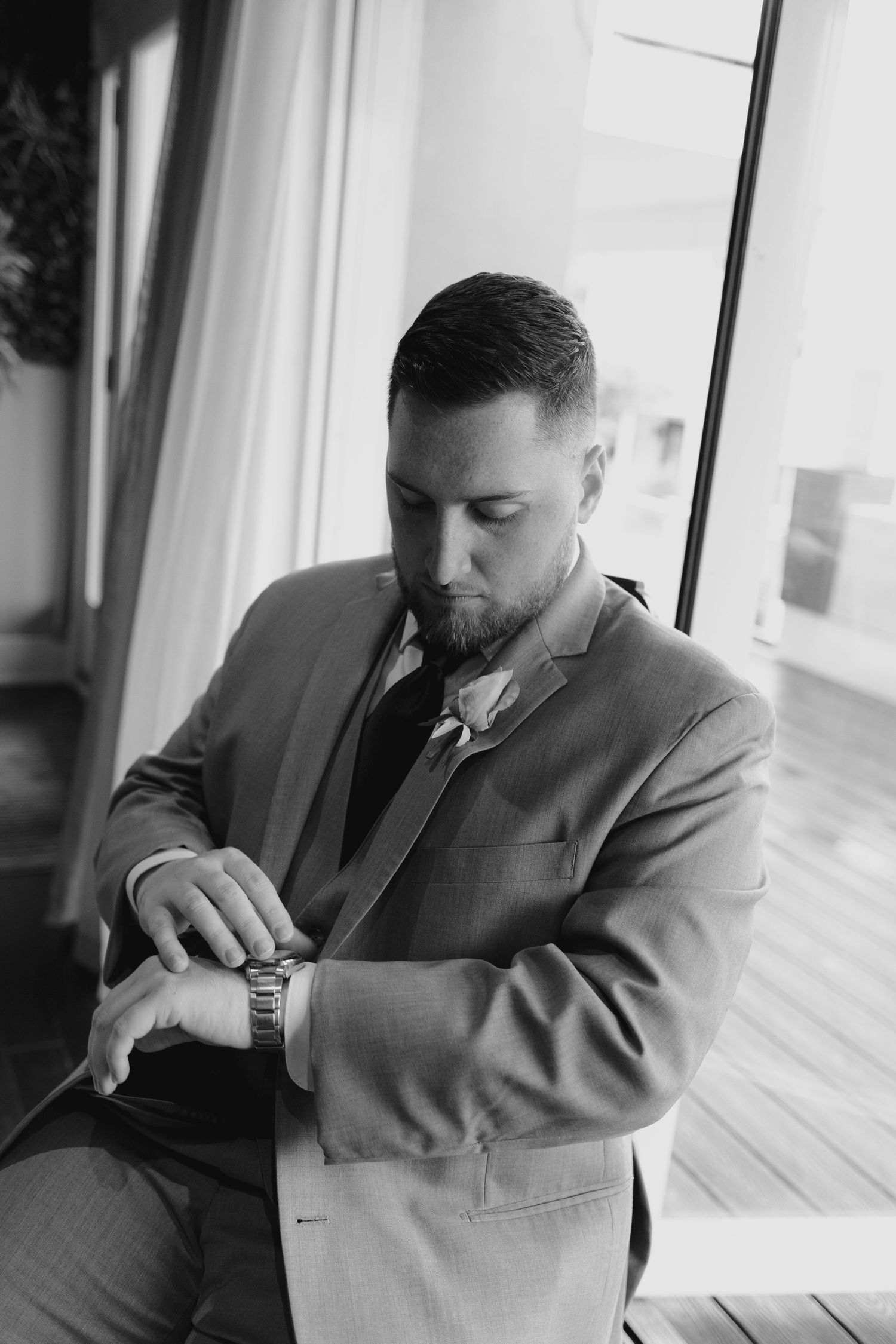 Black and white photo of a groom in a suit checking his watch before the wedding ceremony.