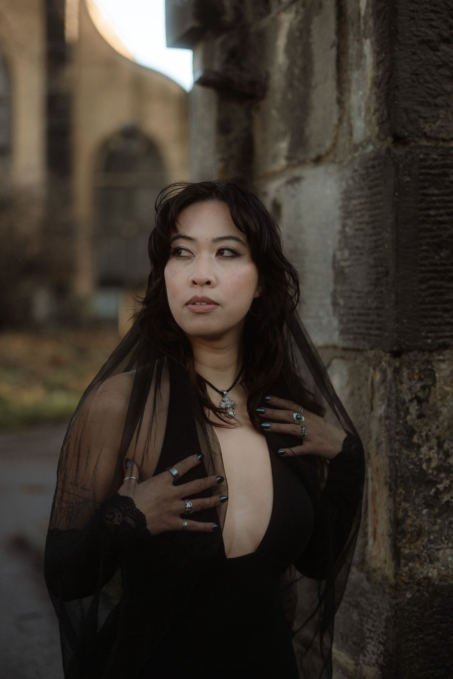 A gothic style portrait in dark tones shows someone posing dramatically against a tree trunk in sheer black clothing.