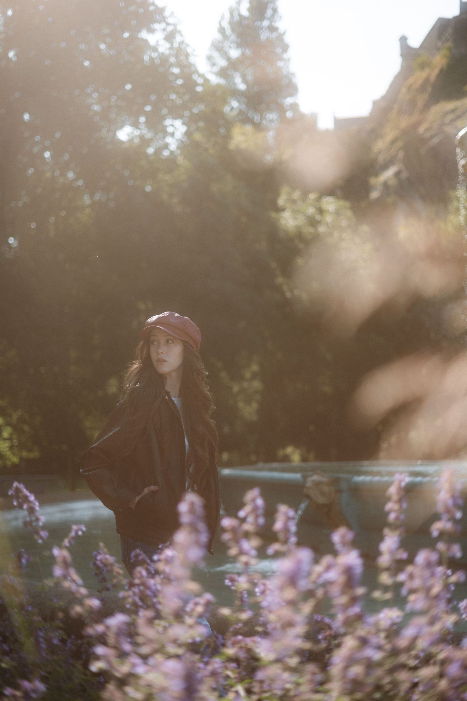 Woman in red beret and black jacket standing among purple wildflowers in golden sunlight.