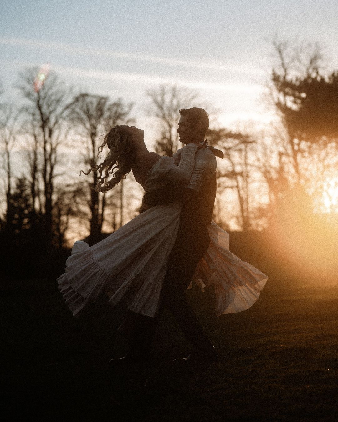 Silhouette of a couple dancing romantically at sunset with golden light and bare trees in the background.