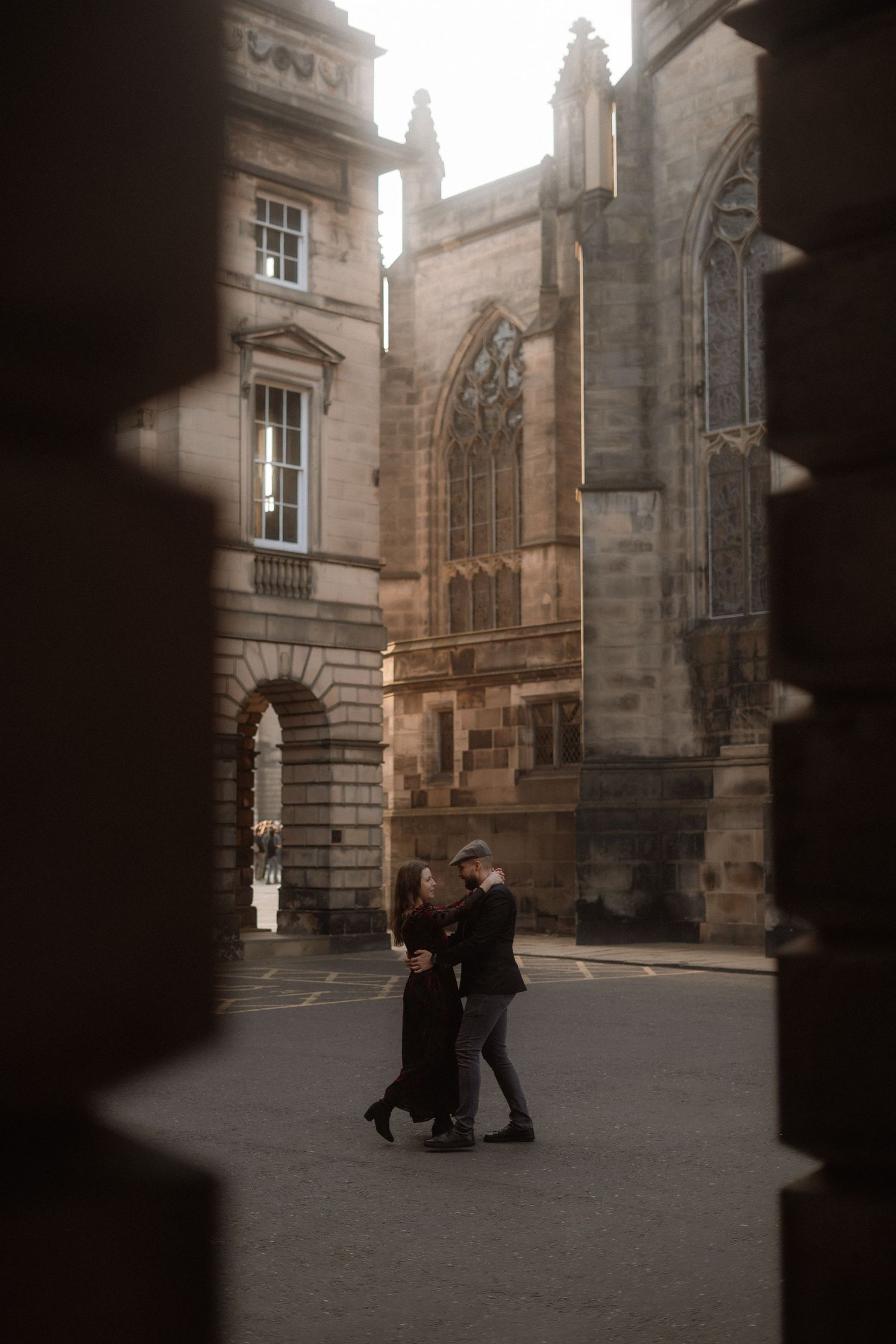 Two people dance in a historic stone courtyard with gothic architecture.