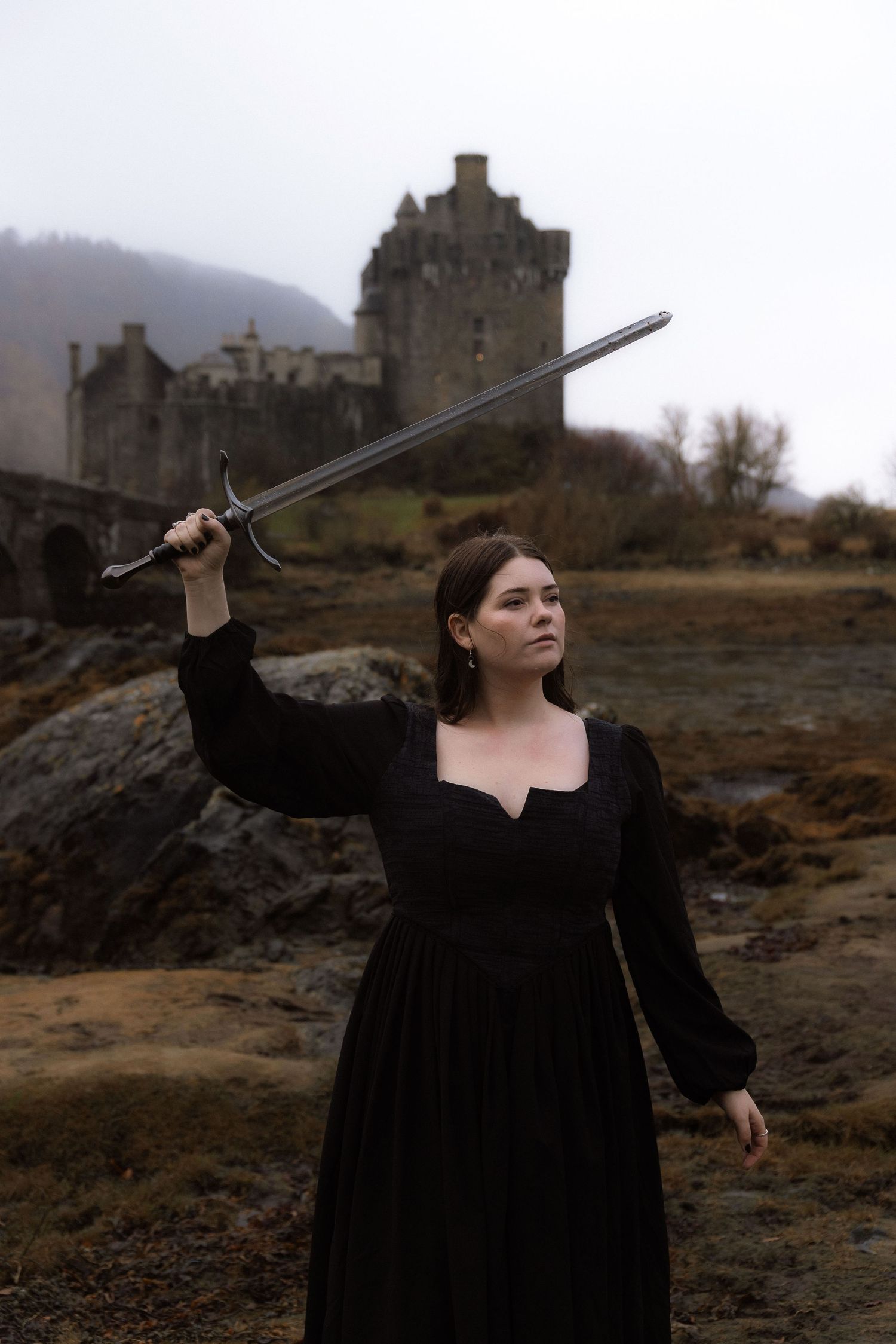 Headshot of photographer Natalie Whelan, hold sword, castle in background, Eilean Donan Castle, Scotland, Skye