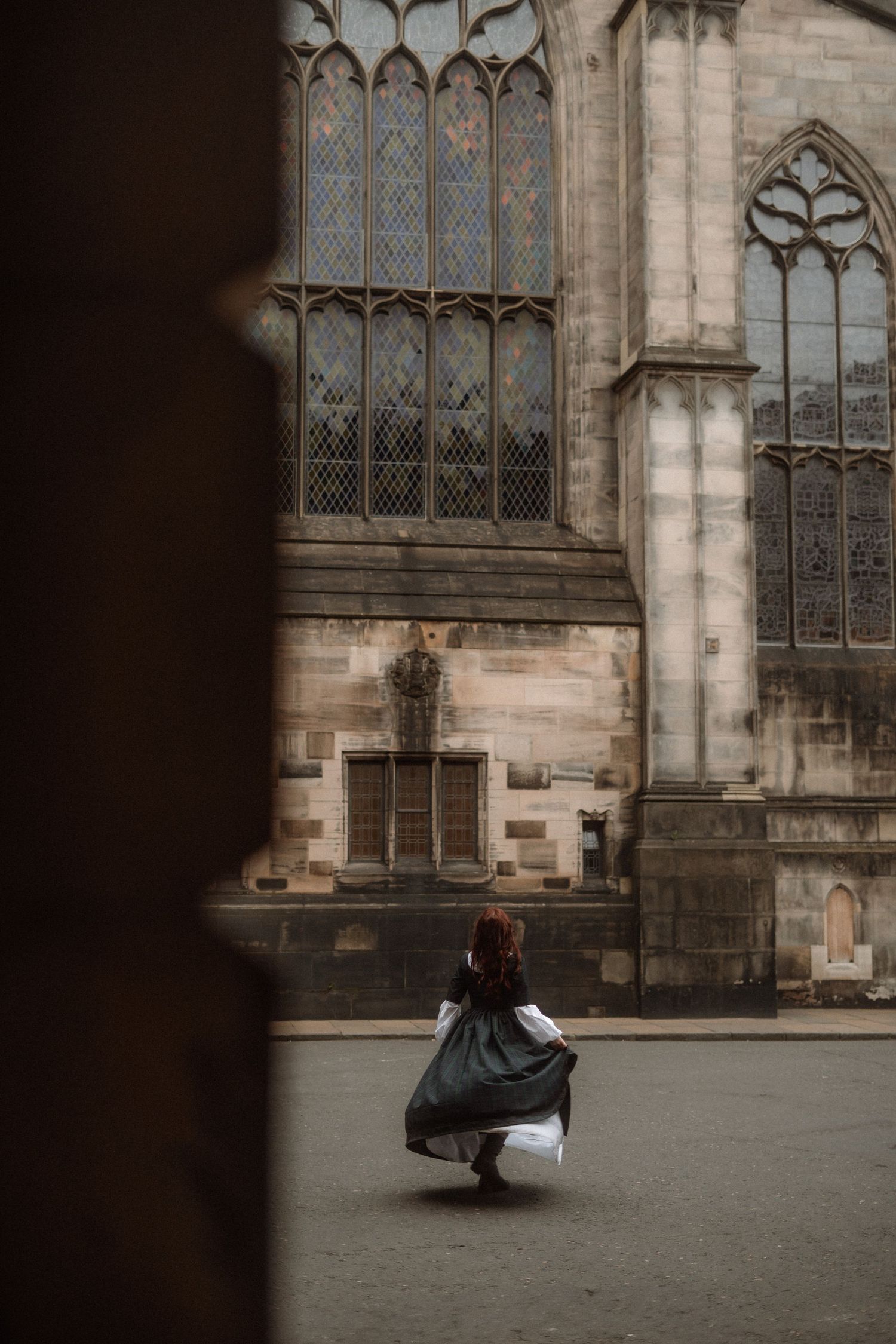 A person in dark clothing twirls gracefully against the backdrop of a Gothic cathedral's stone walls and stained glass windows.