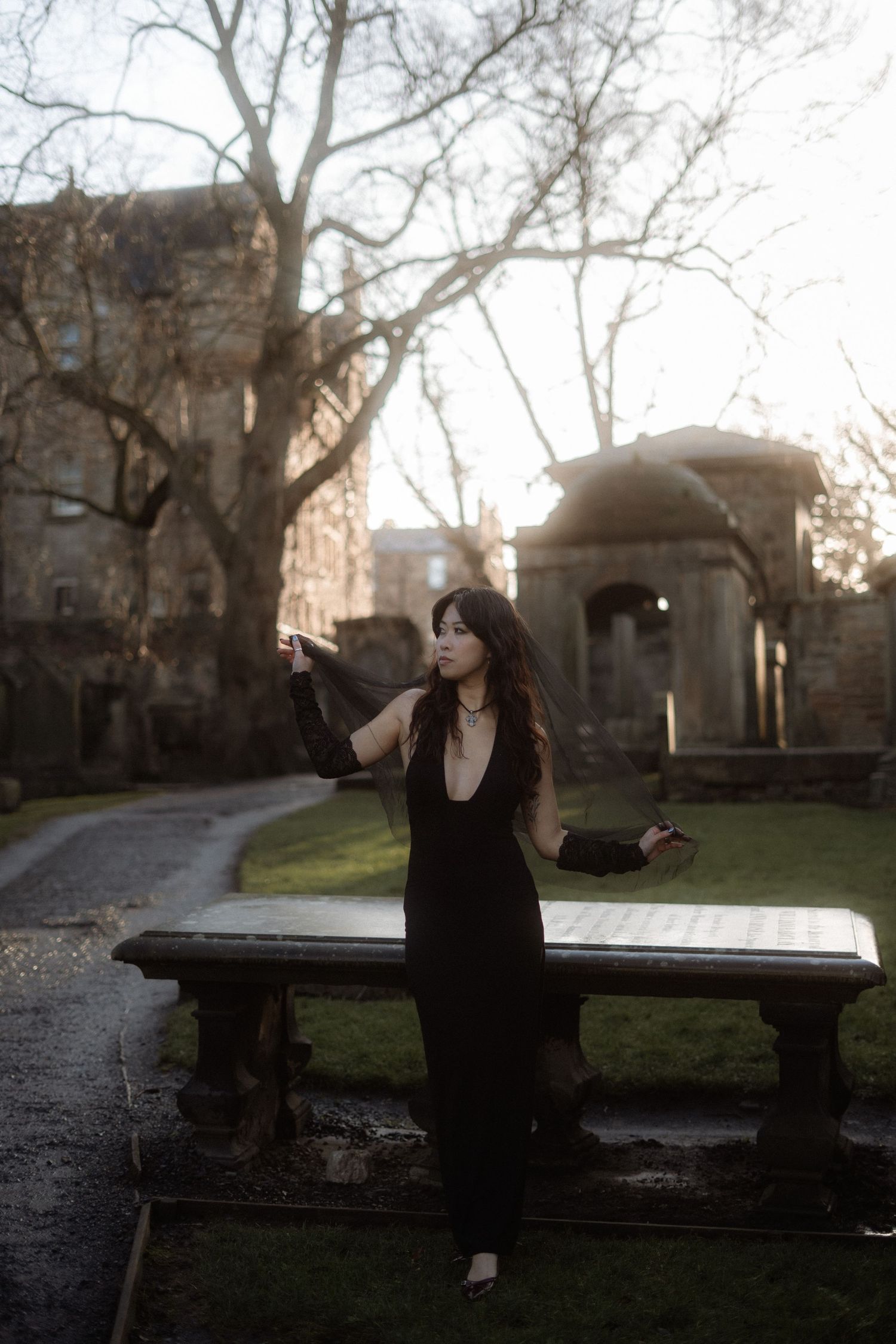 A series of four moody black and white photos showing someone in dark clothing sitting on stone structures in a garden setting.