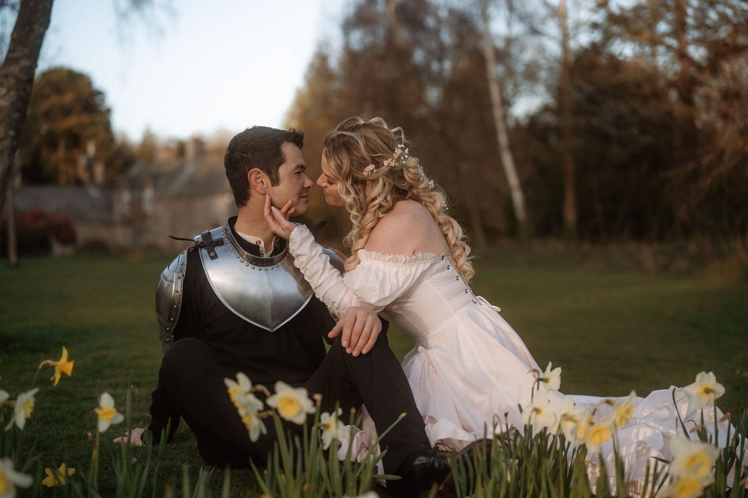 Bride and groom kissing among daffodils, groom in knight armor and bride in white wedding dress outdoors.