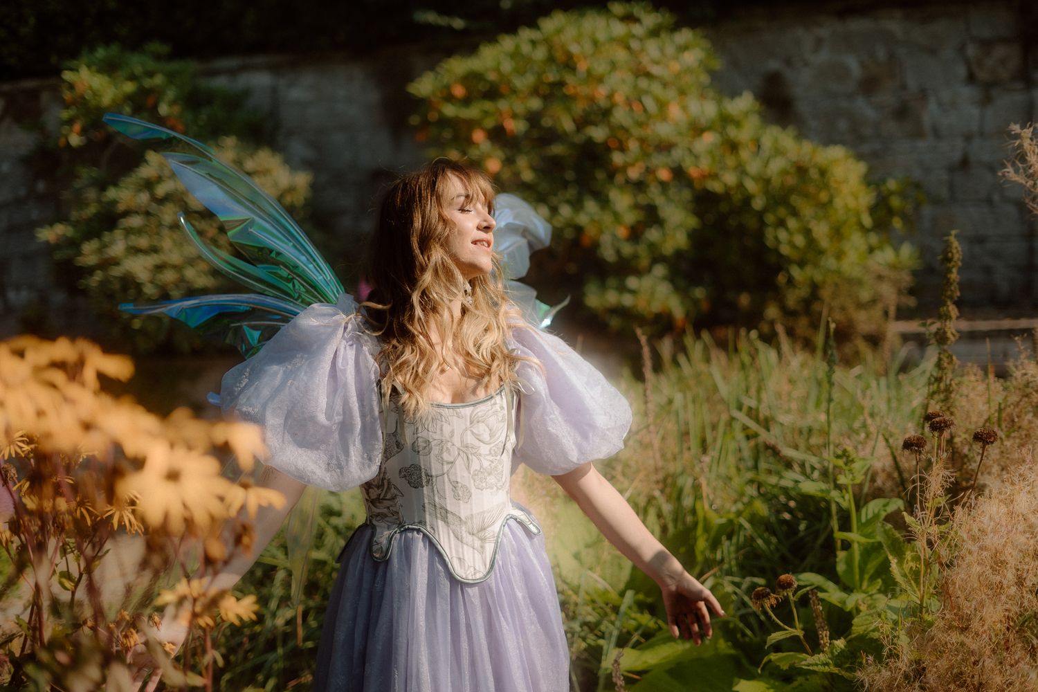 A figure in a flowing lavender dress dances gracefully through a sunlit garden setting.
