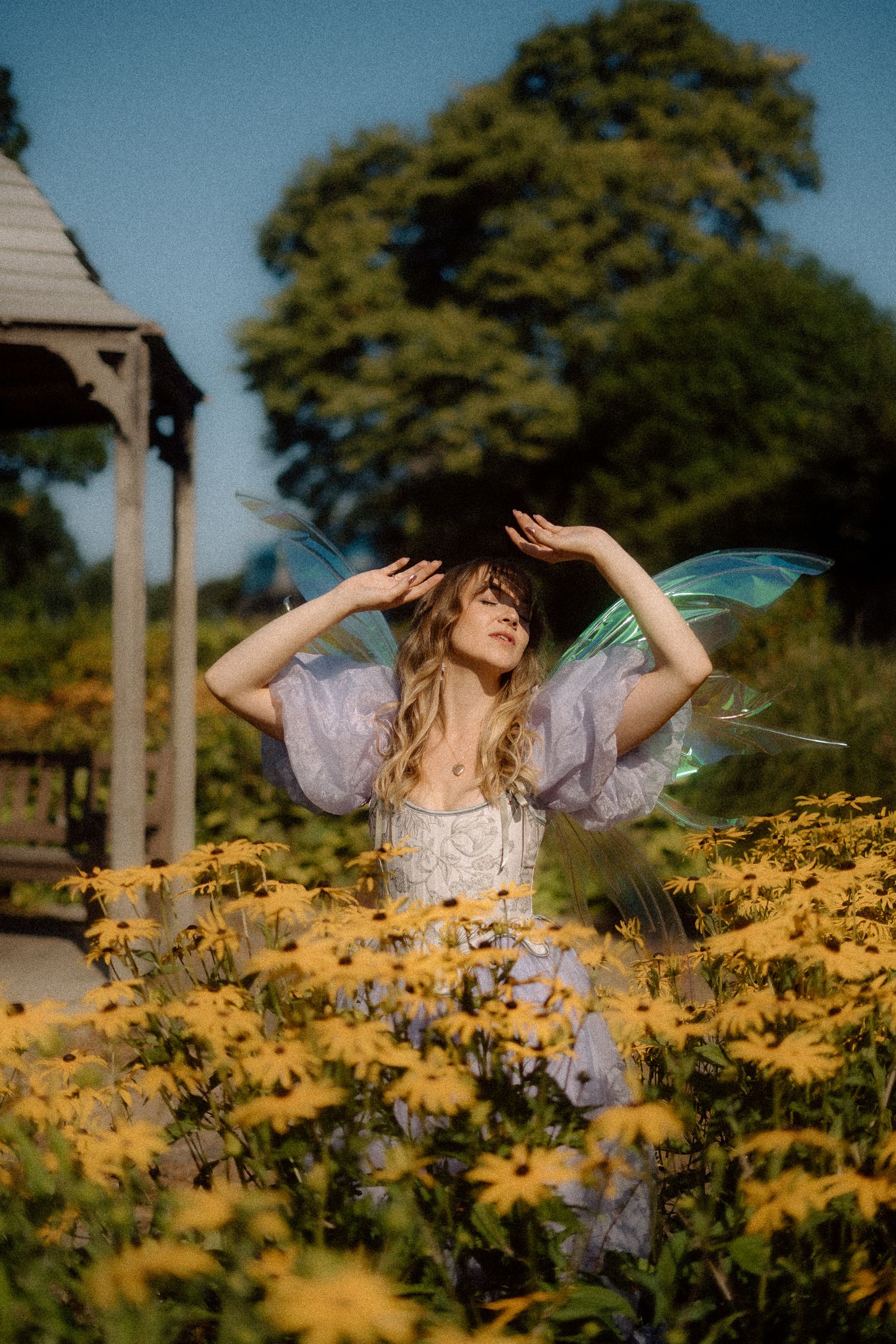 Ethereal figure in lavender dress dances gracefully among blooming yellow flowers in a sunlit garden setting.