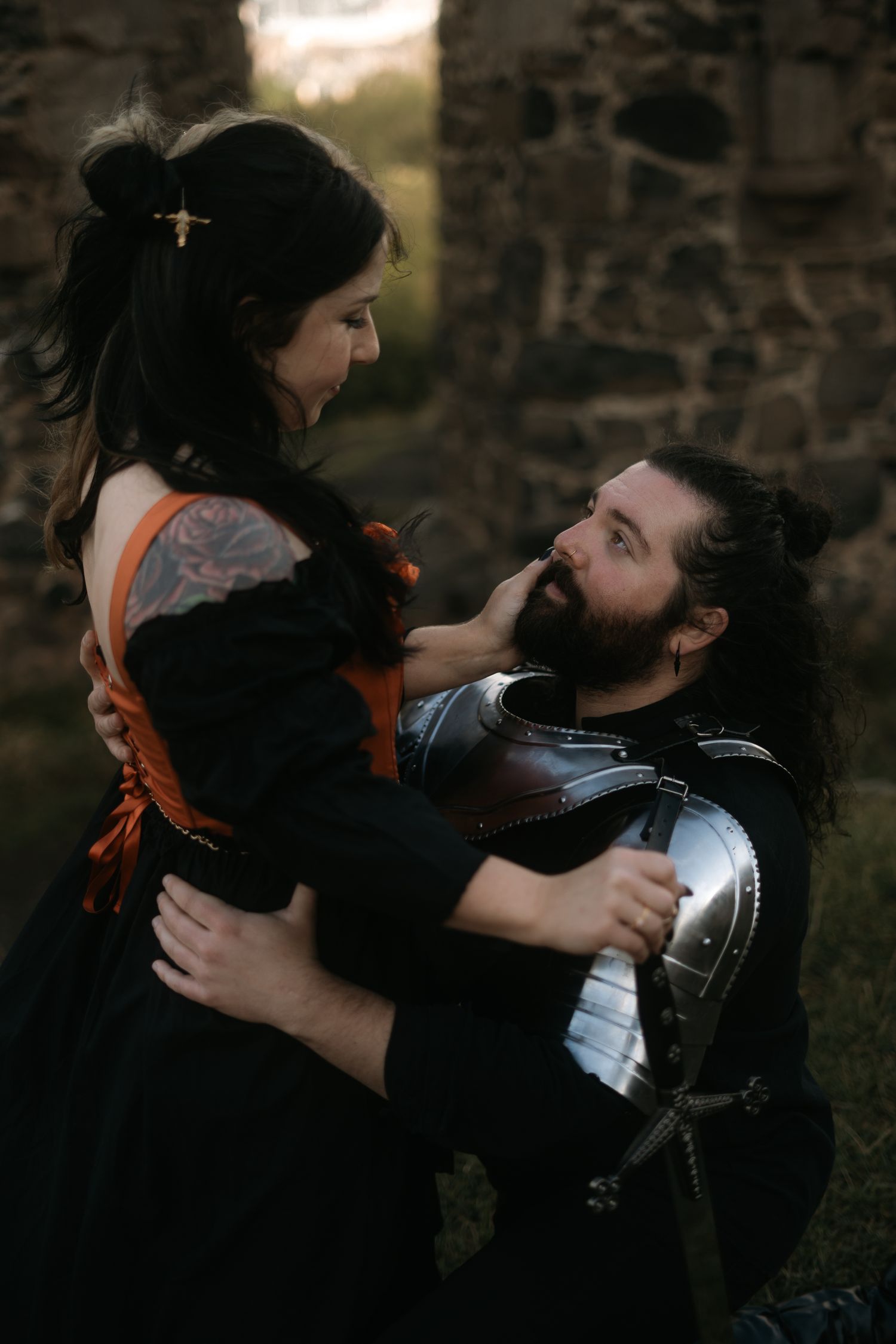 Couple hold each other in front of a ruin, man in knight armour and woman dressed in ren faire attire, St Anthony's Chapel, Edinburgh