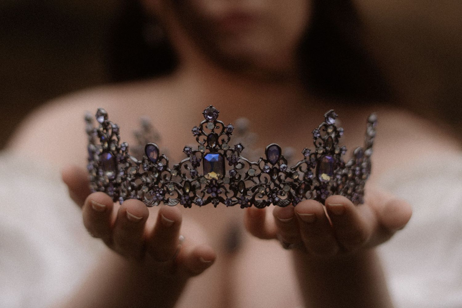 Close up of woman in white dress and dark hair blowing in wind, holds up a purple and silver tiara, Glencoe,  Scotland