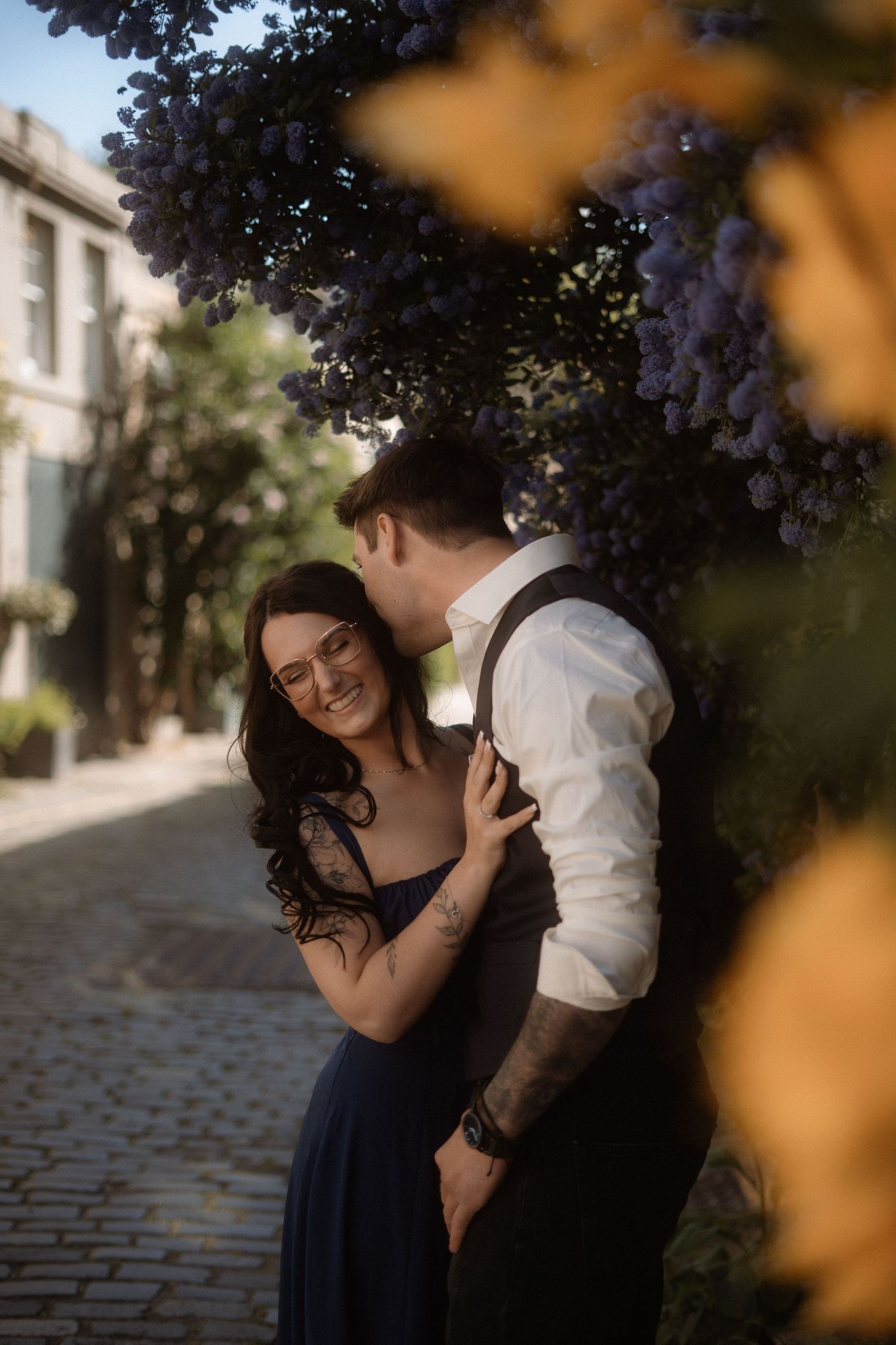 A couple shares a tender moment under autumn trees on a cobblestone street.