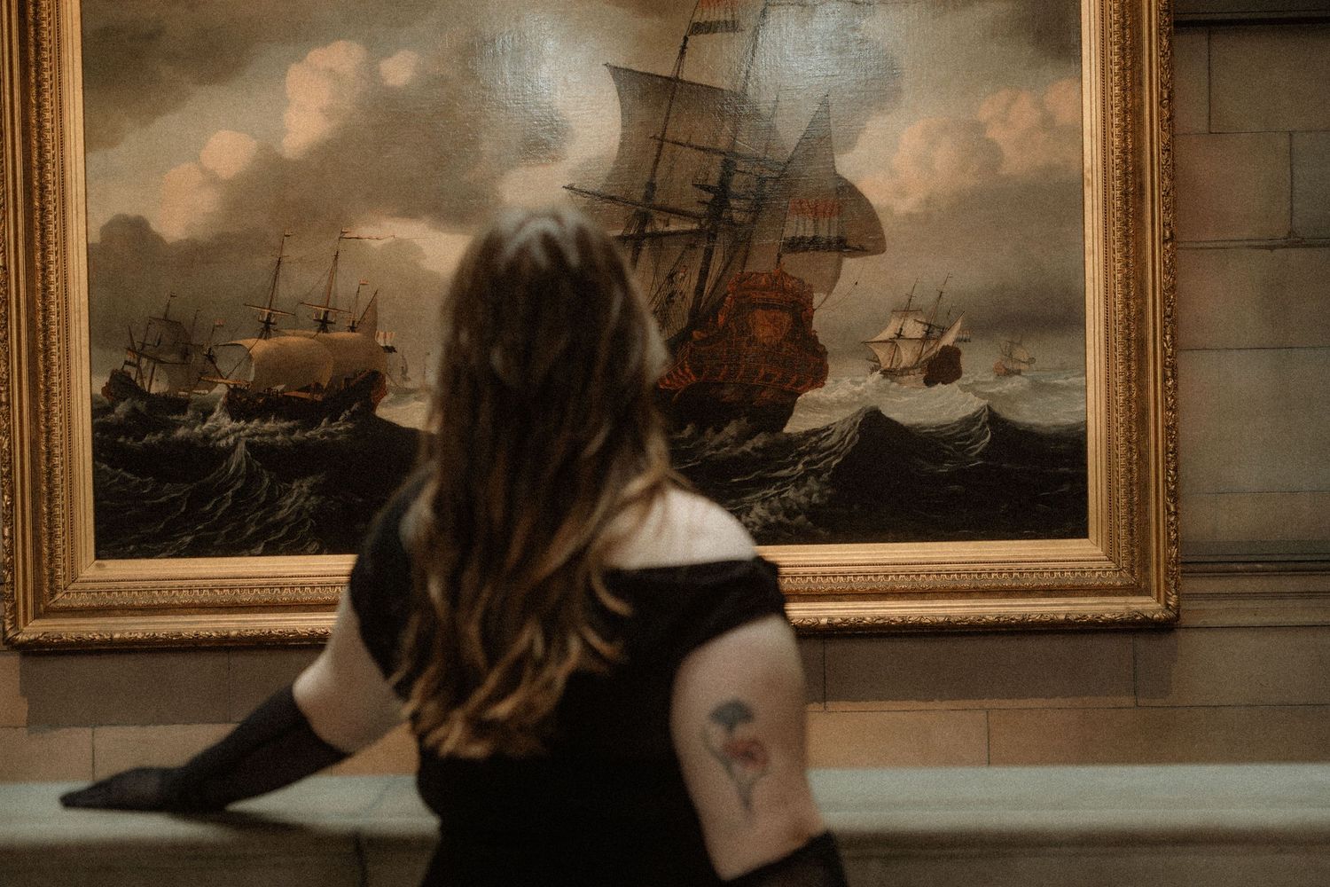 Elegant woman dressed in black with black gloves and pearls, stands next to an painting in an art gallery, Kelvingrove Art Gallery, Glasgow