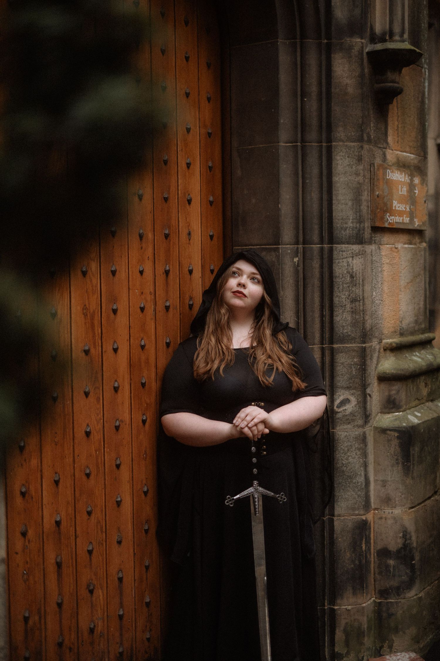 A dark and moody portrait series against a medieval wooden door and stone wall with dramatic lighting and a sword prop.