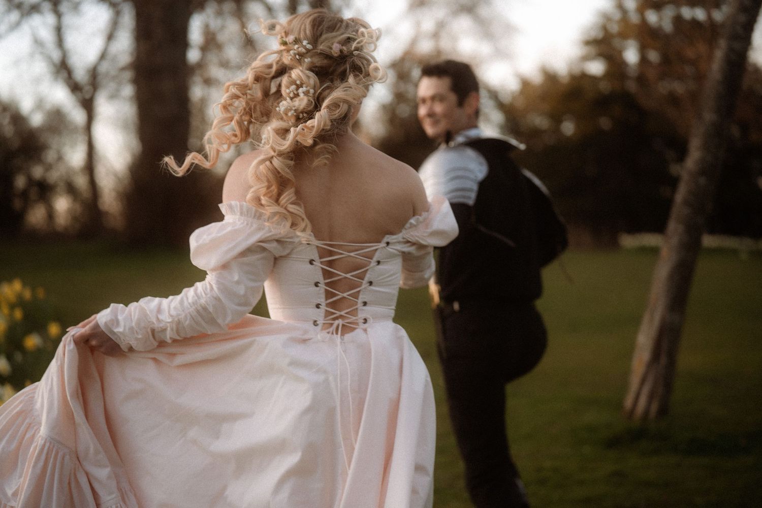 Bride in lace-up corset wedding gown dancing with groom outdoors in garden at golden hour.