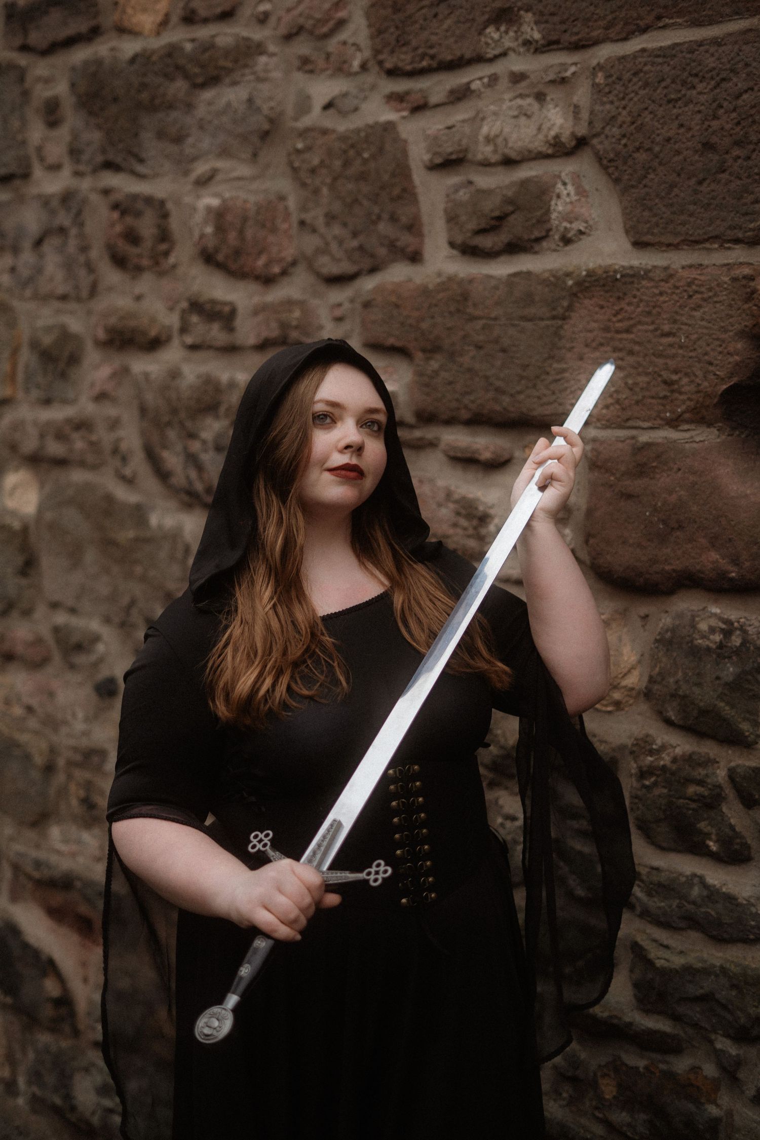 A person in black clothing poses with a sword against a stone wall in a series of dramatic shots.
