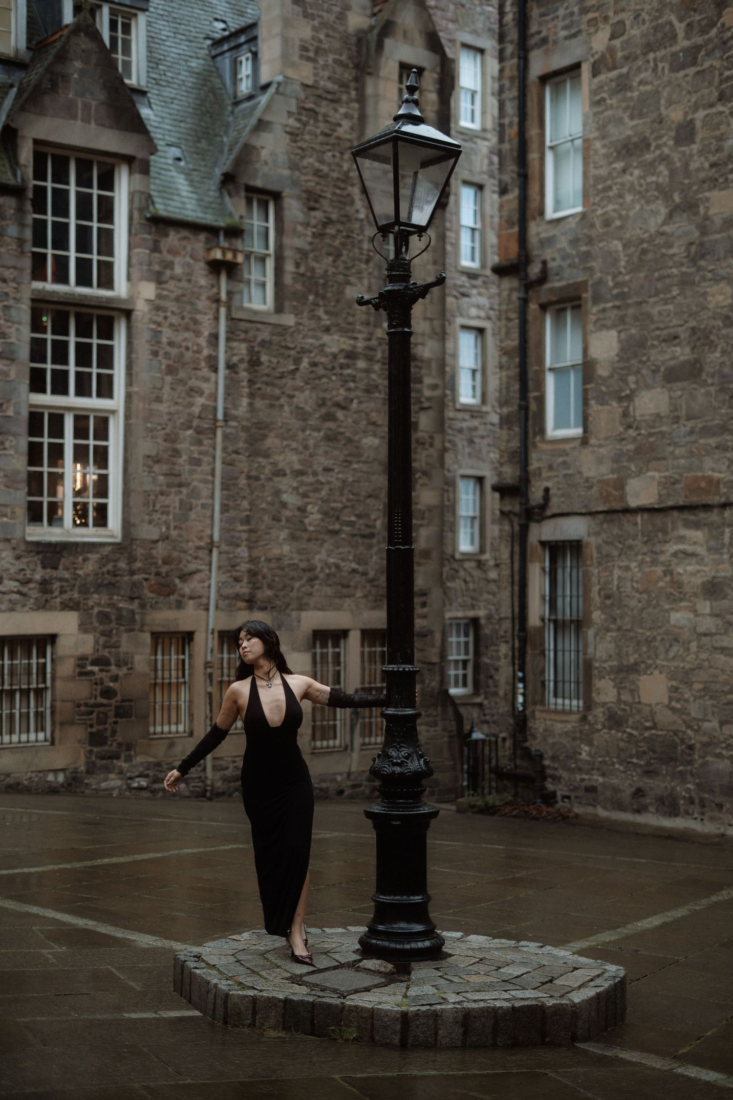 A person in black stands in a historic courtyard with stone walls and traditional lanterns in Edinburgh, Scotland.