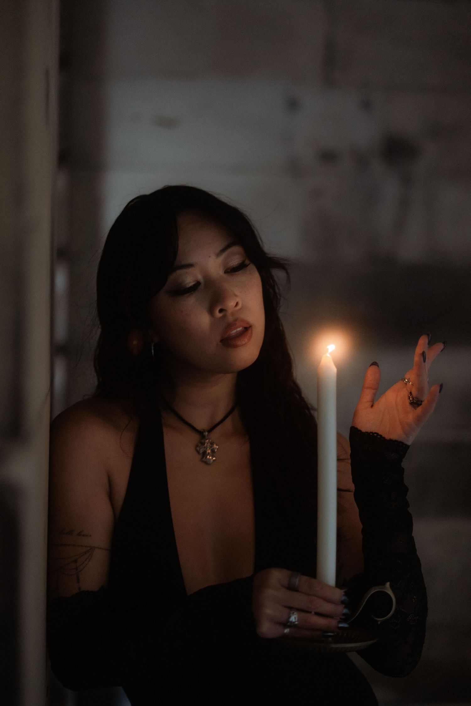 A moody candlelit portrait features a person in black attire with a pendant necklace in a dark atmospheric setting.