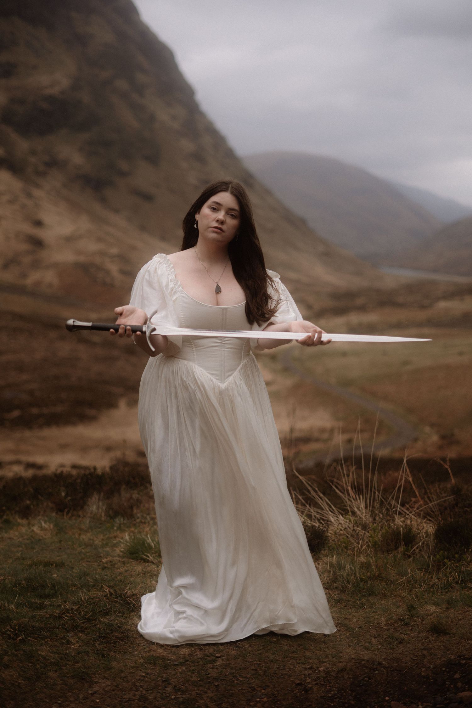 Self portrait of photographer Natalie Whelan, white dress, holding sword, glencoe landscape, Scotland