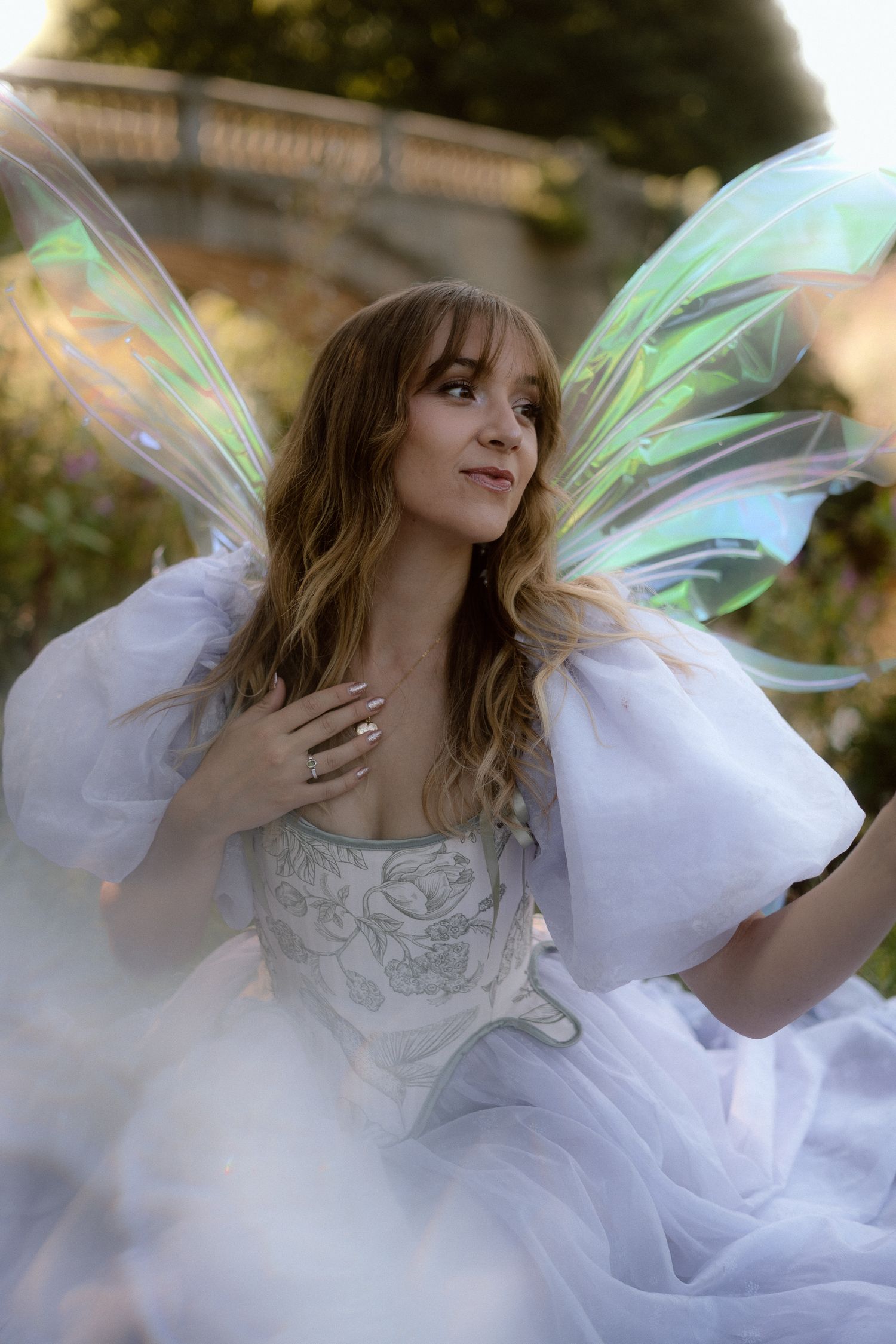 Ethereal figure in flowing white dress with iridescent fairy wings dances gracefully in a dreamy outdoor setting.