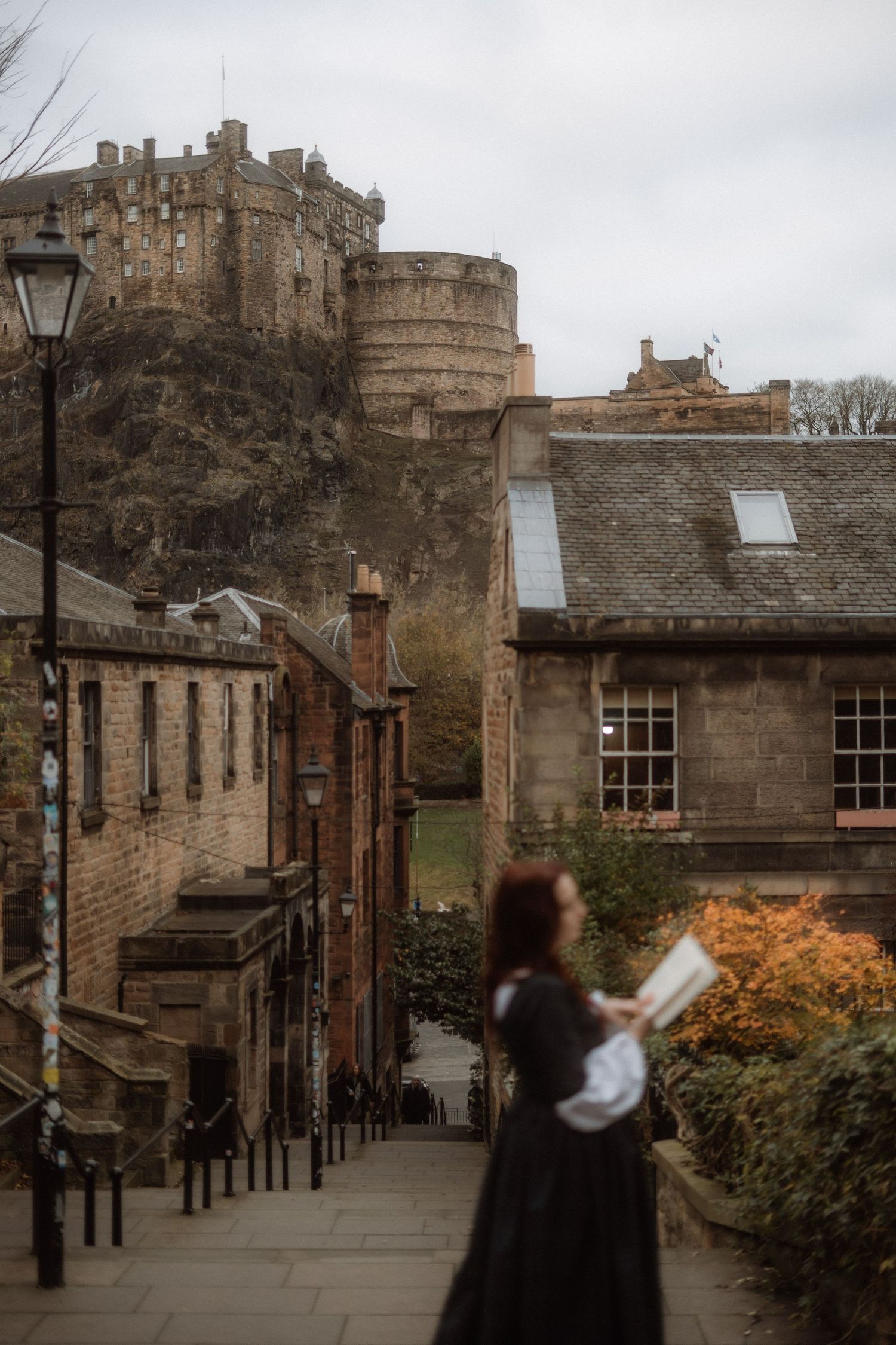 Historic stone buildings and walkways at Edinburgh Castle on a cloudy day with autumn foliage visible.
