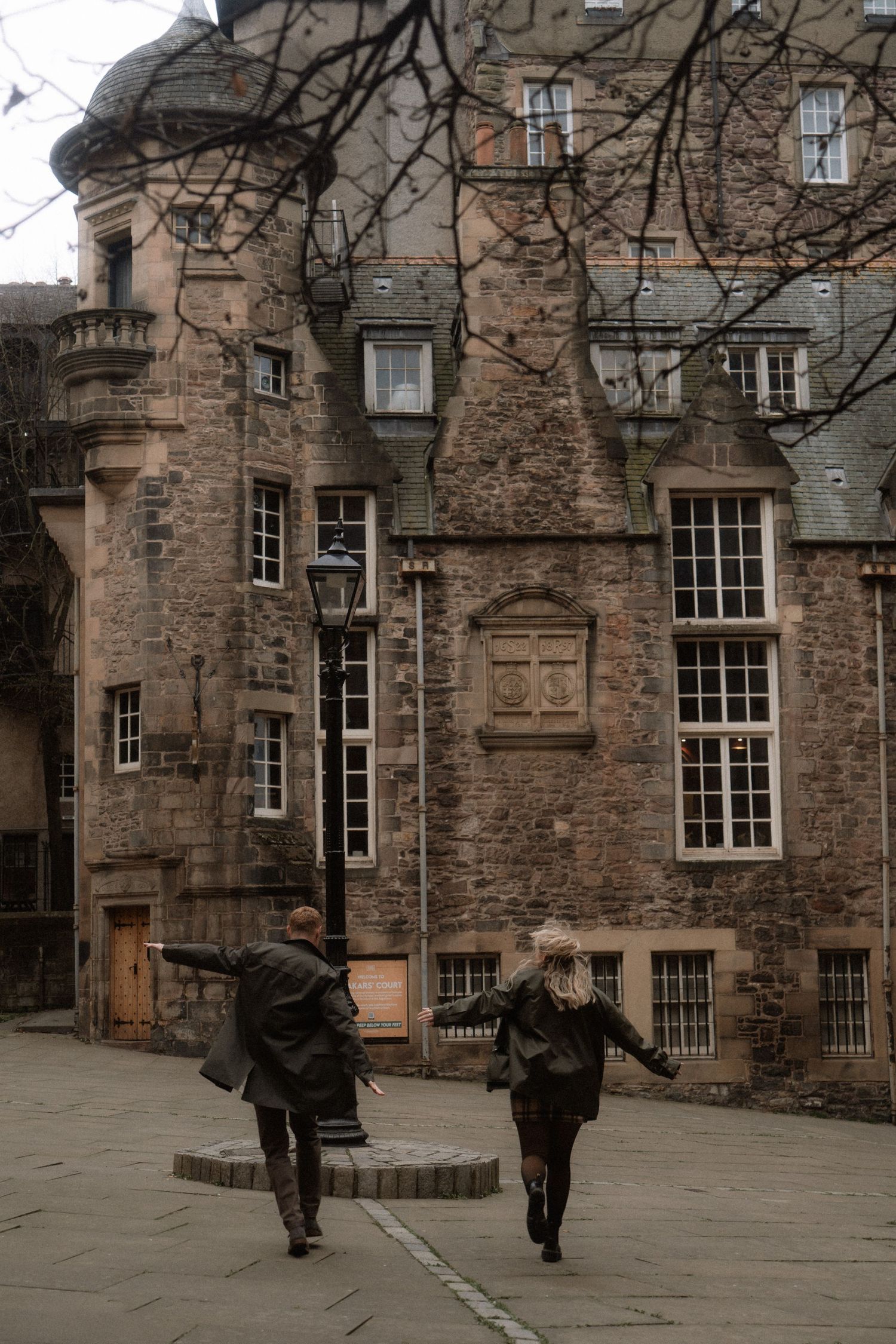 Couple walking through an old Edinburgh courtyard with historic stone architecture.