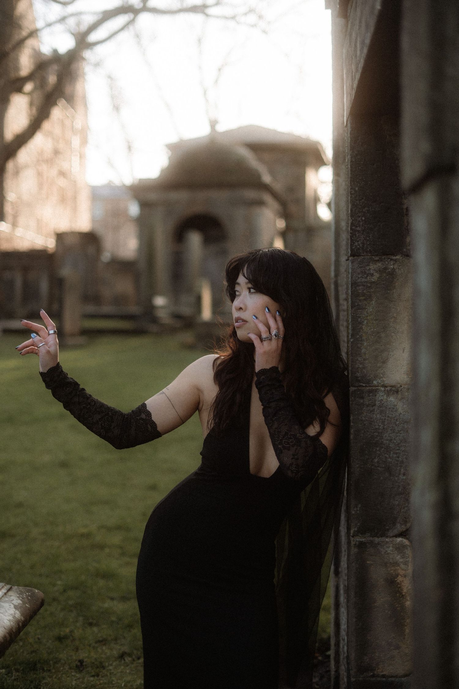 A person in dark clothing poses dramatically between stone pillars in a moody outdoor setting at dusk.