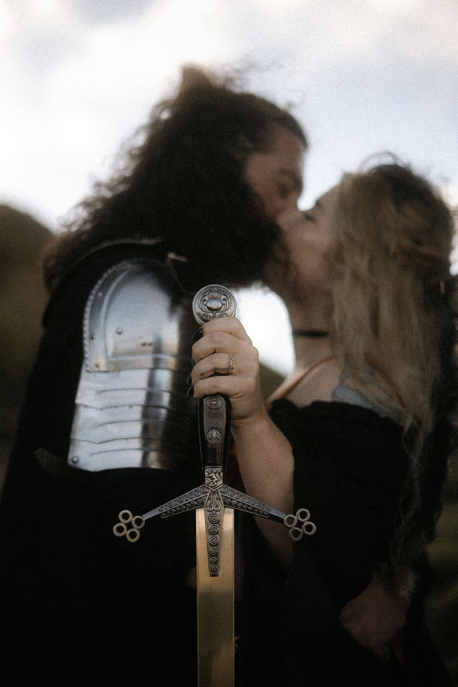 Couple hold each other in front of a ruin, man in knight armour and woman dressed in ren faire attire, St Anthony's Chapel, Edinburgh