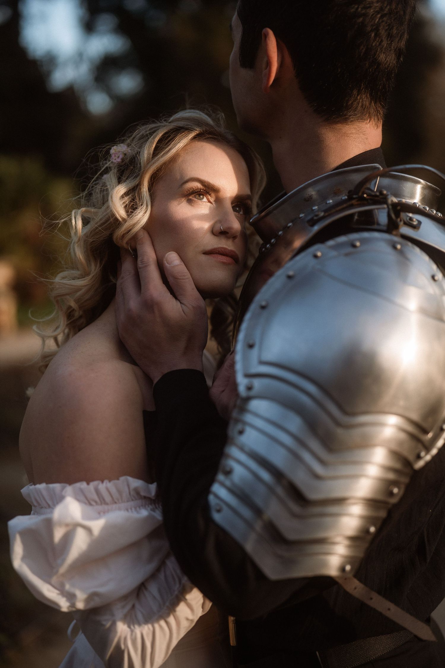 A knight in shining armor tenderly cups a blonde woman's face in a romantic medieval fantasy portrait.