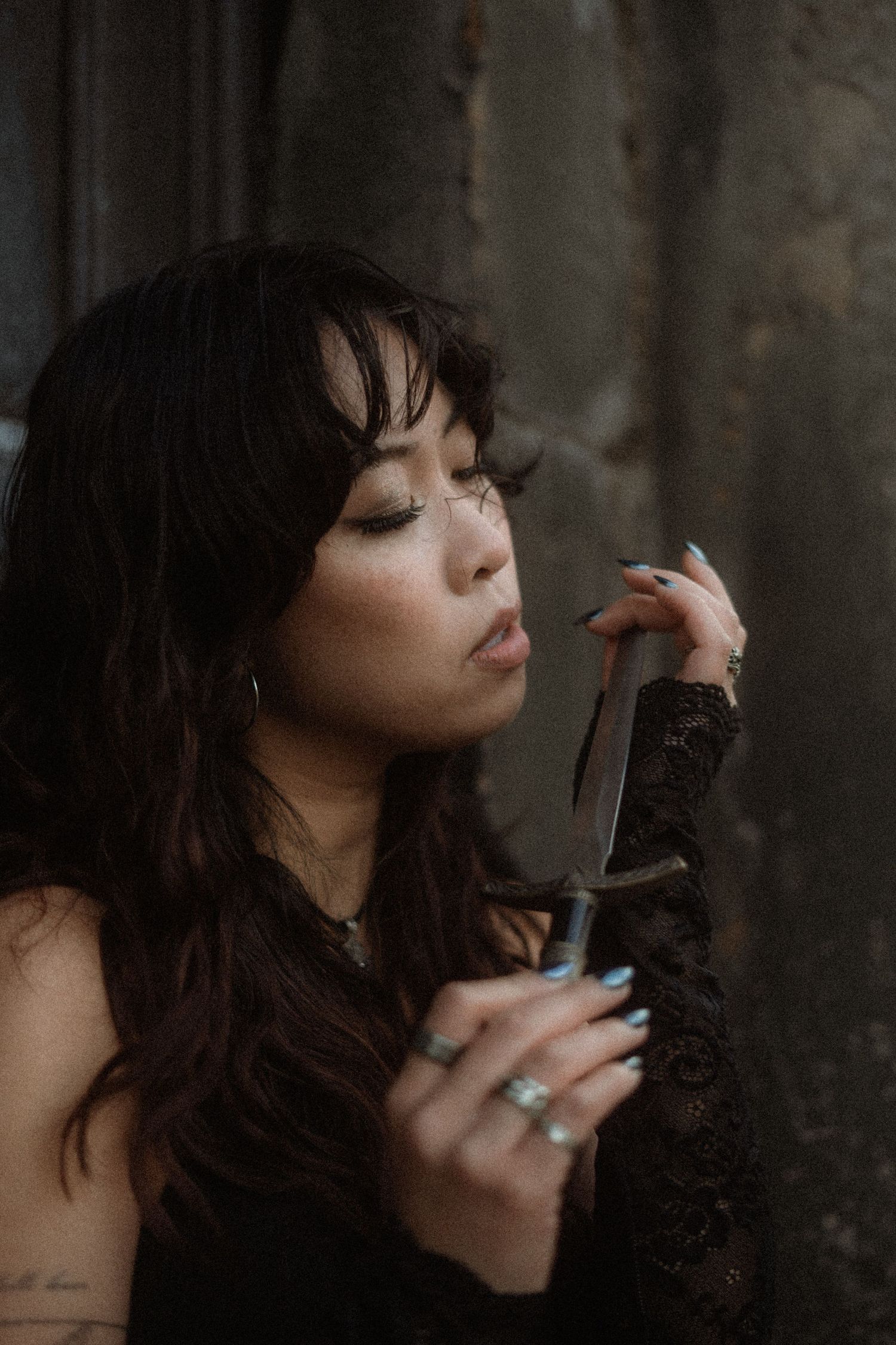 A woman with dark wavy hair exhales smoke in a moody artistic photo series.