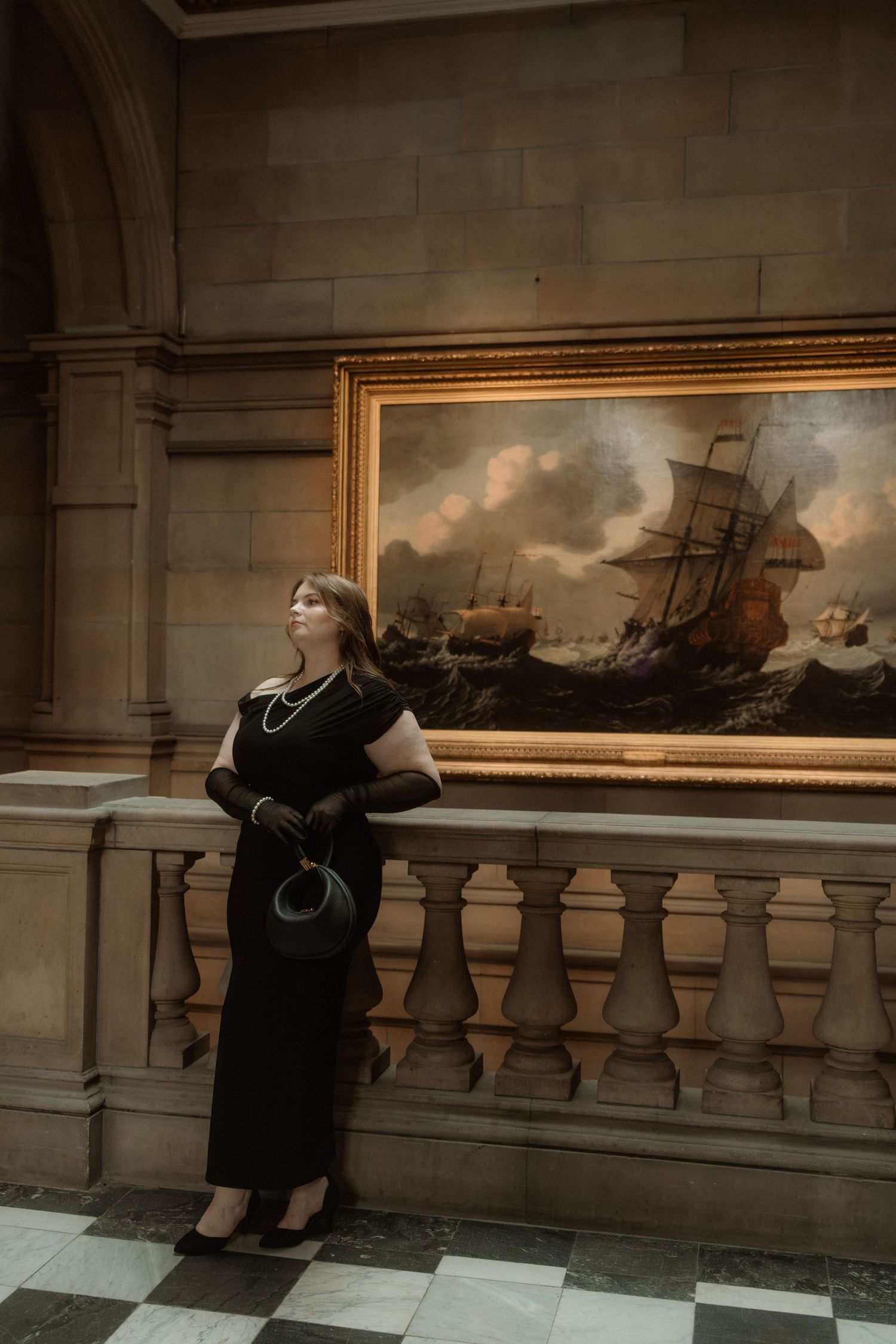Elegant woman dressed in black with black gloves and pearls, stands next to an painting in an art gallery, Kelvingrove Art Gallery, Glasgow