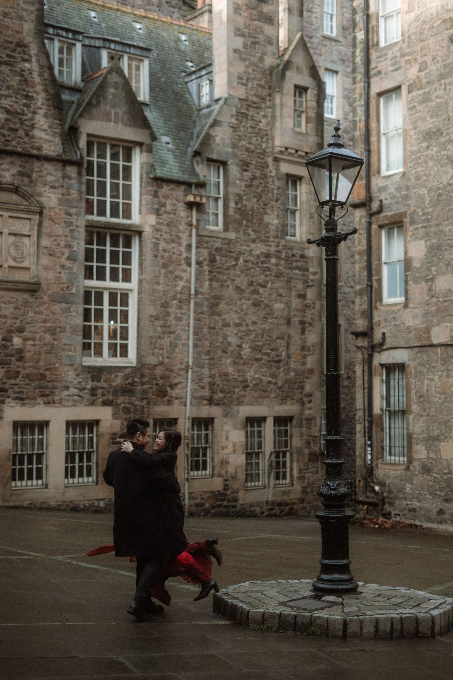 Two figures dance in an atmospheric stone courtyard surrounded by historic architecture.