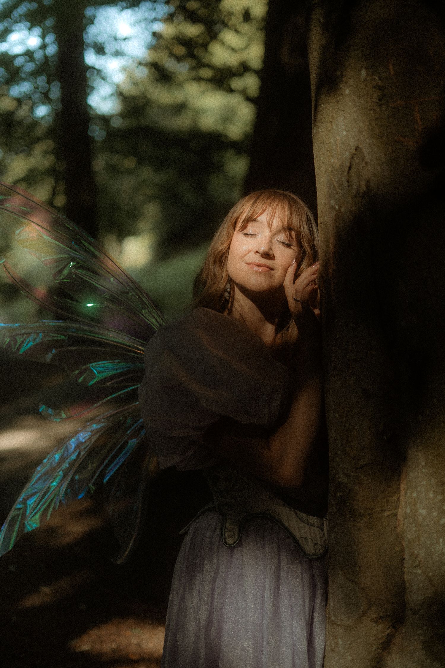 A dreamy artistic portrait in a forest with ethereal fairy wings and soft natural lighting creating a magical atmosphere.