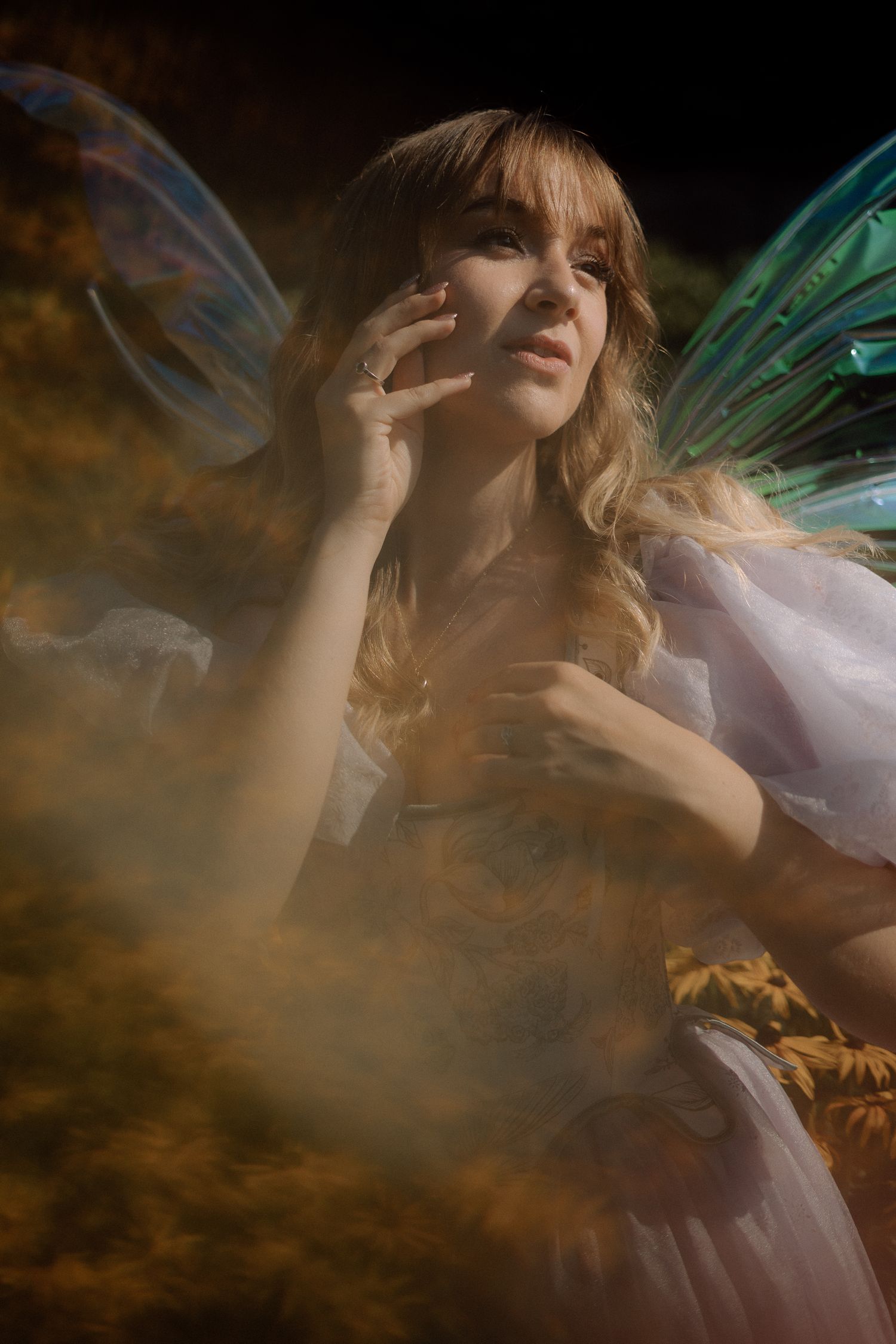 Ethereal fantasy portrait of a figure in soft lighting with fairy wings and flowing fabric surrounded by misty atmosphere.