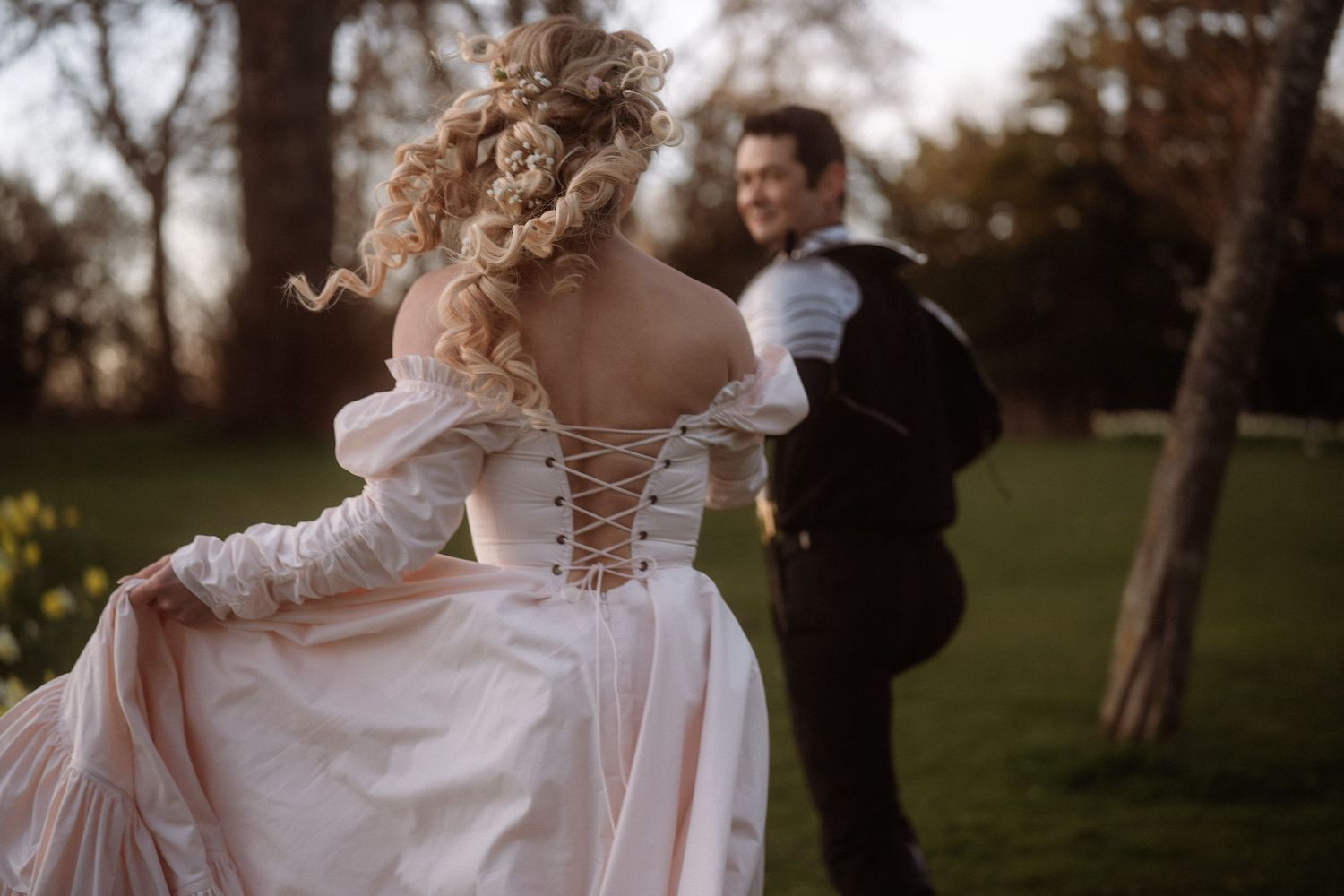 Bride in a pink lace-up corset wedding gown dances with groom in a lush garden at golden hour.