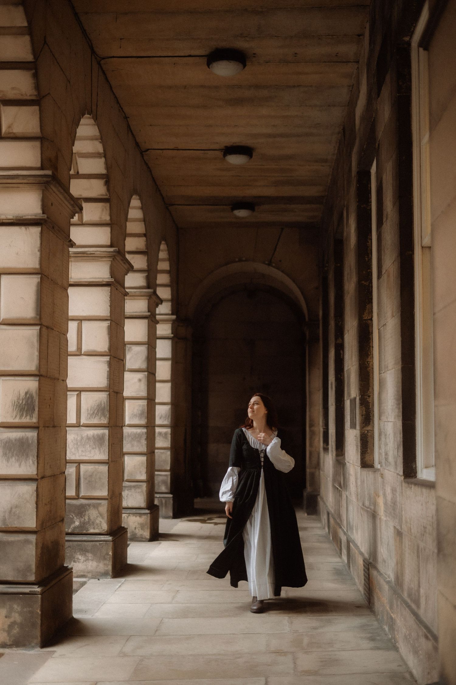 A person walks through a historic stone colonnade with arched pillars and dramatic shadows in a classical building.