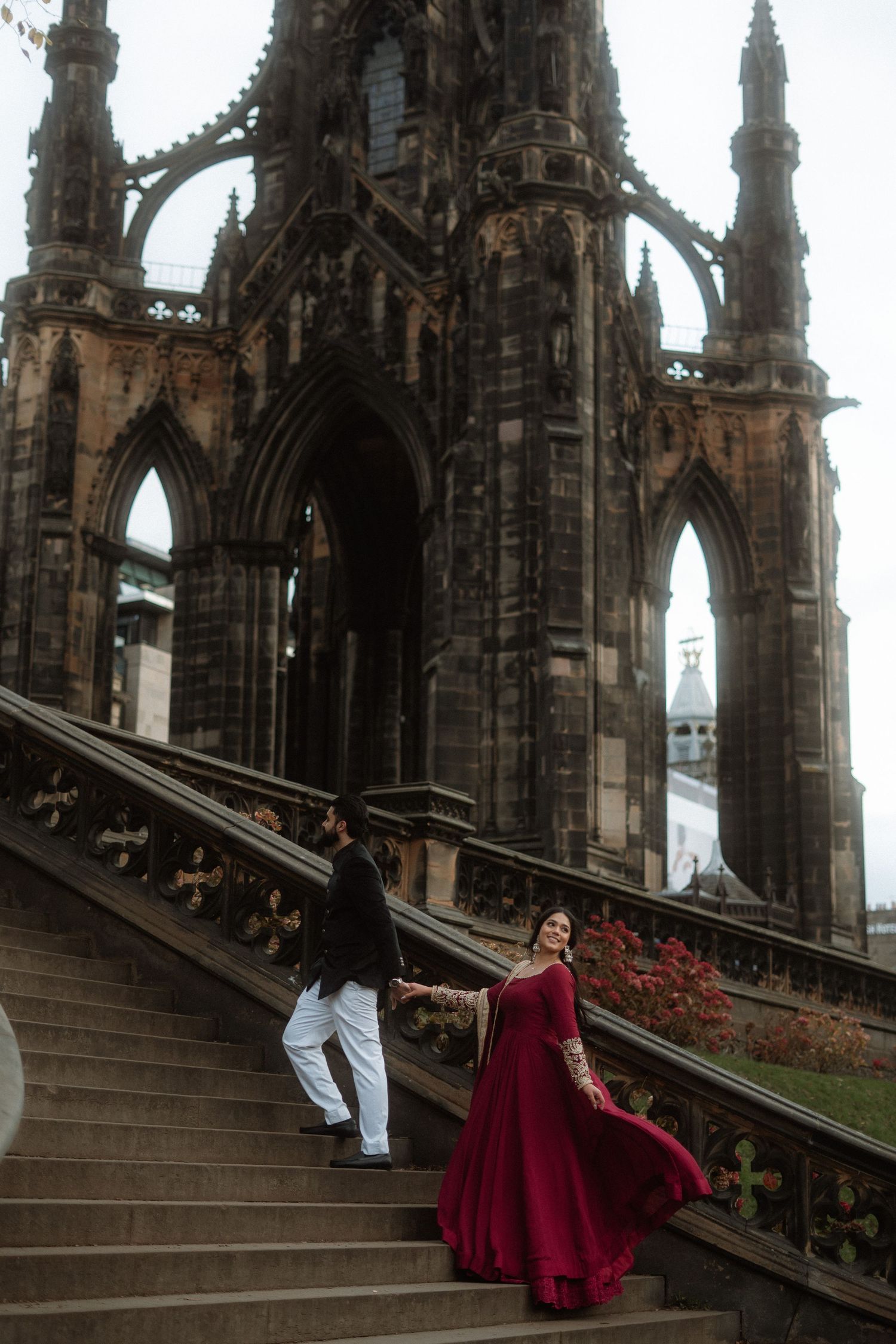 Couple dramatically pose on staircase, Woman in red dress, Scott Monument in Edinburgh, Scotland.