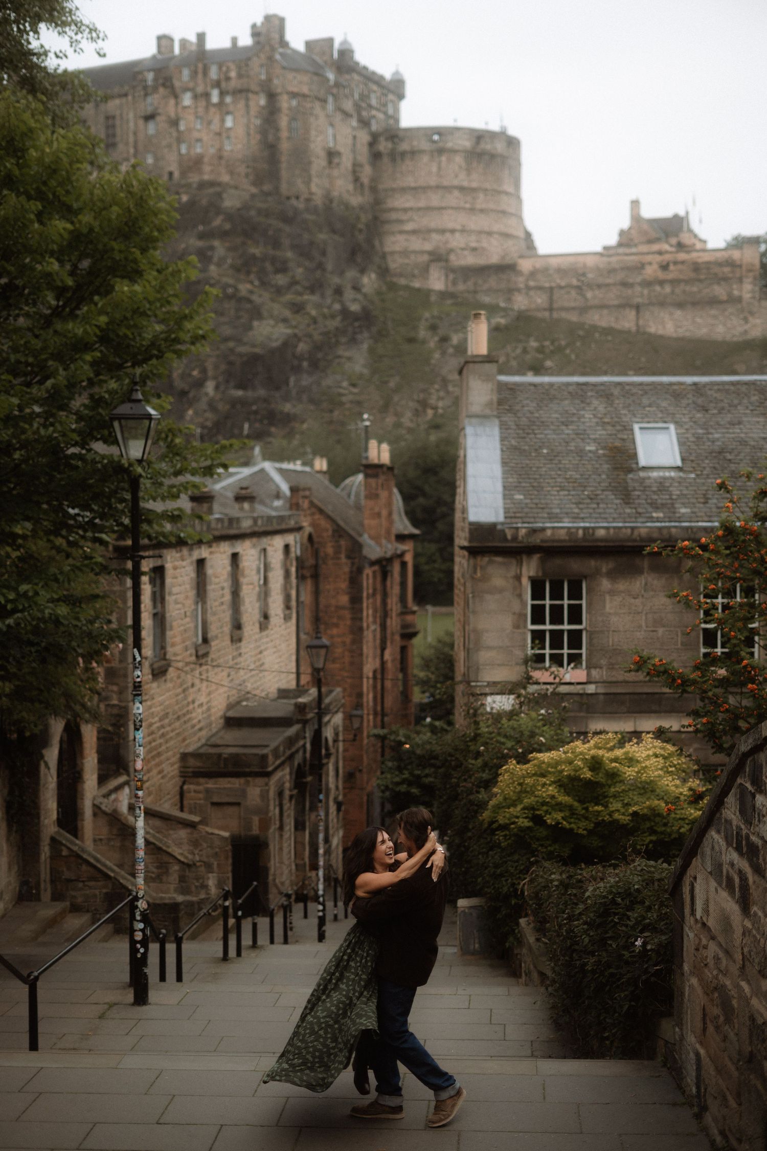 Couple dancing romantically on historic Edinburgh street with castle backdrop and stone buildings.
