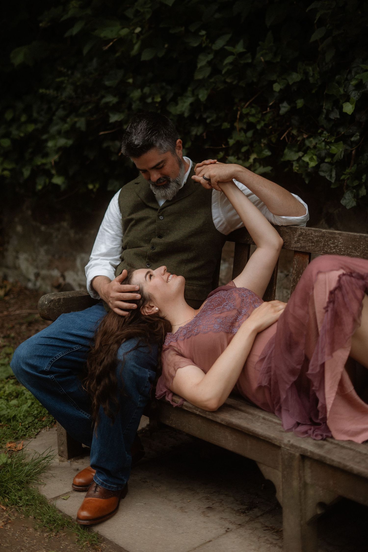 A romantic couple shares an intimate moment on a wooden bench in a garden setting.