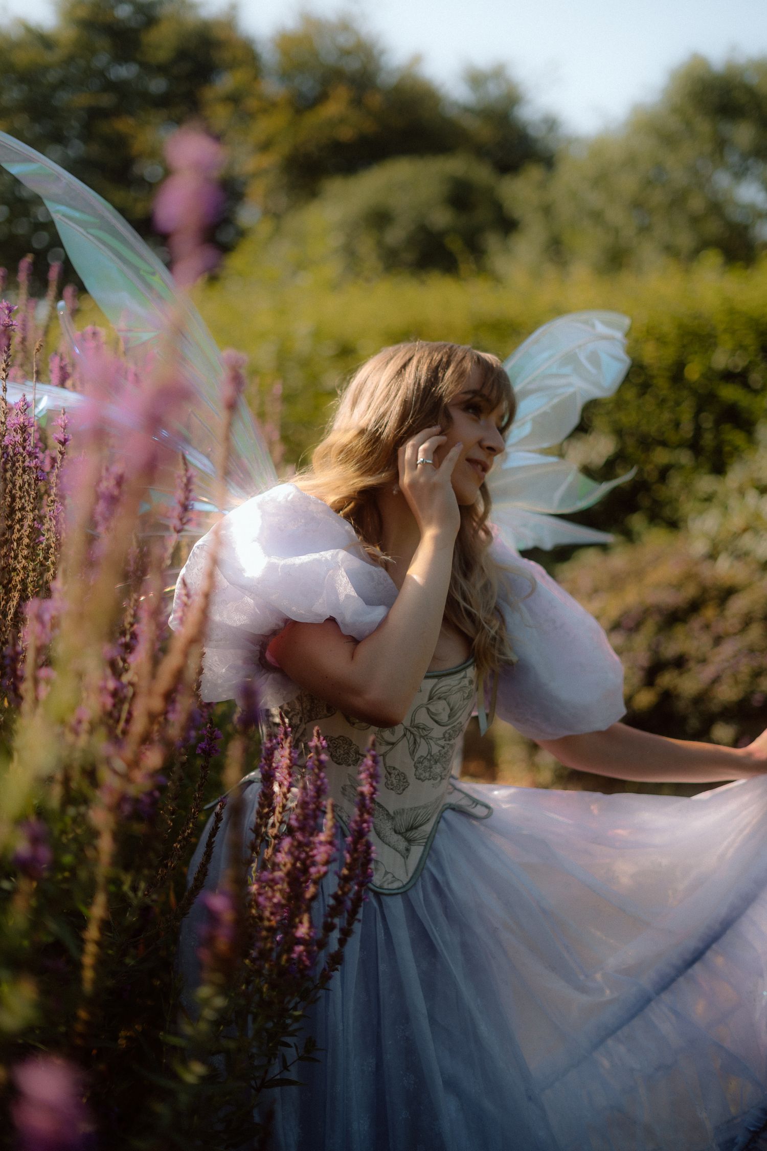 Ethereal figure in white dress and blue skirt twirls gracefully among pink flowers in a sunlit garden.