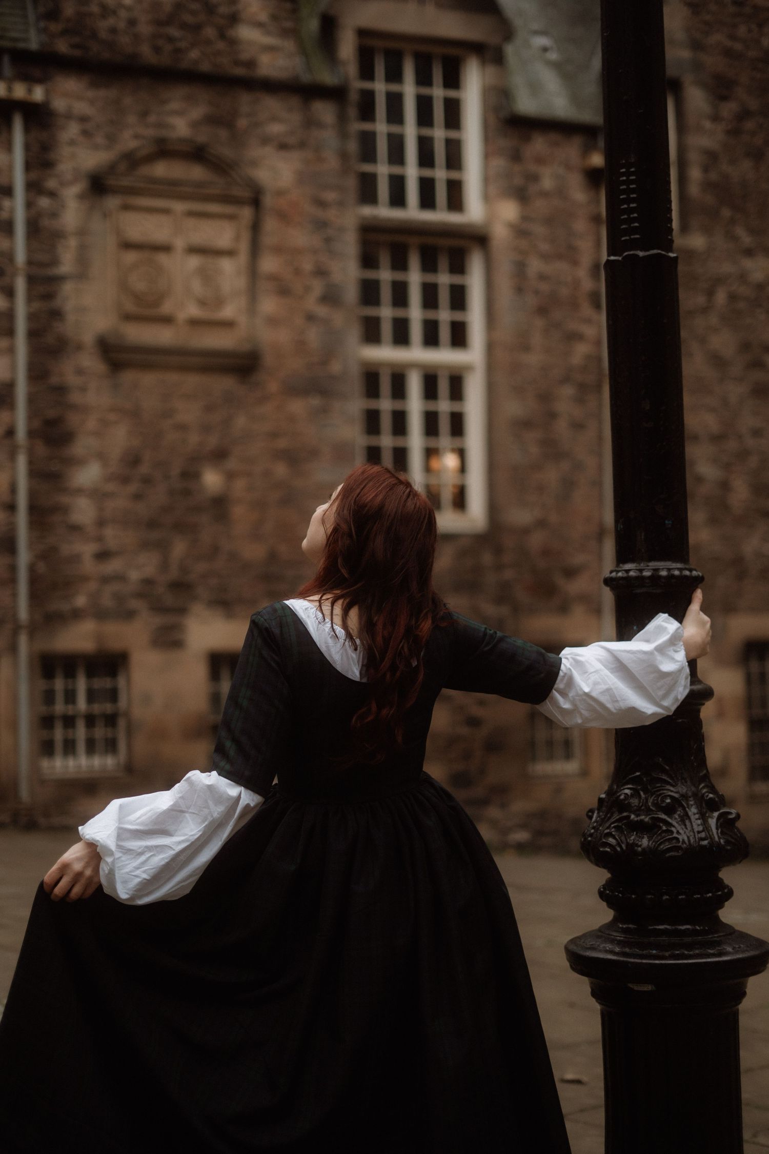 A sequence of four similar images showing a person in black robes leaning against an ornate lamp post outside a historic building.