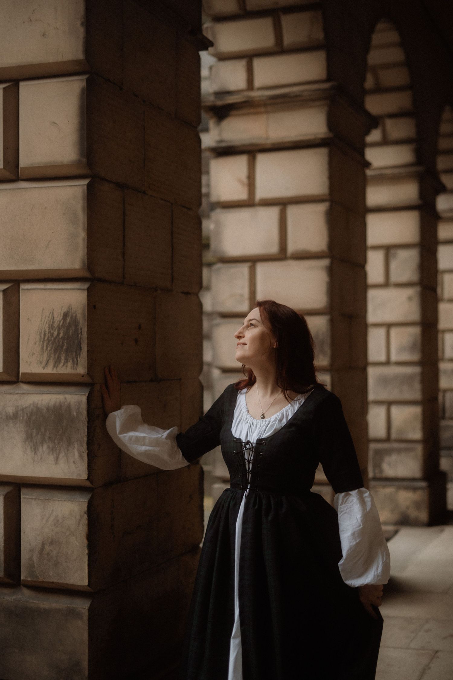 A person in a vintage black and white dress poses elegantly against stone pillars in a historical building.