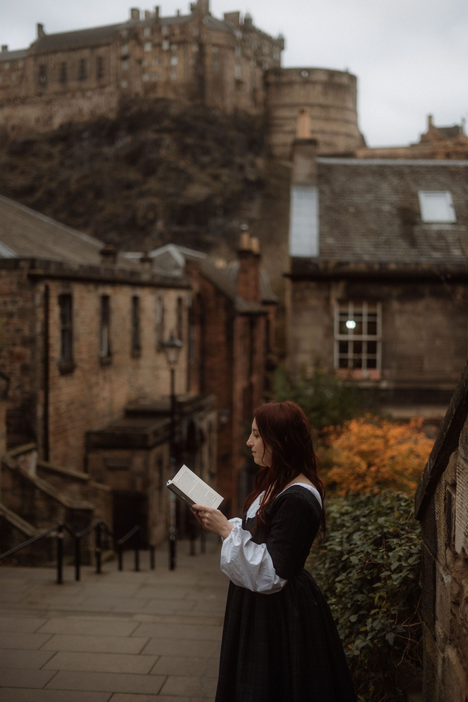 A series of moody photos at Edinburgh Castle showing a person reading against historic stone architecture and autumn foliage.