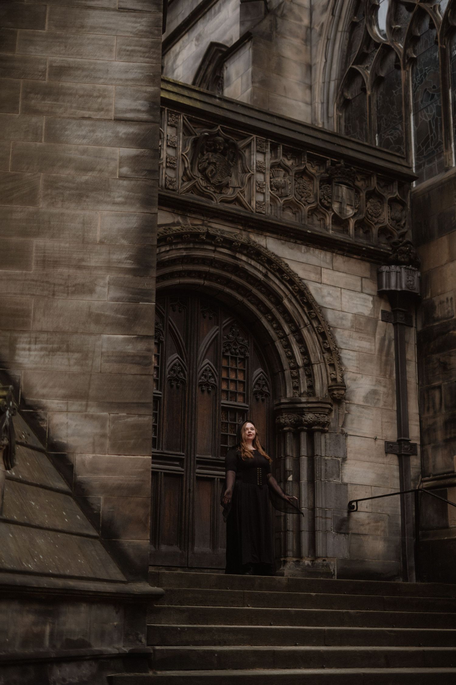 Gothic stone archway entrance with steps and ornate architectural details cast in moody dramatic lighting.