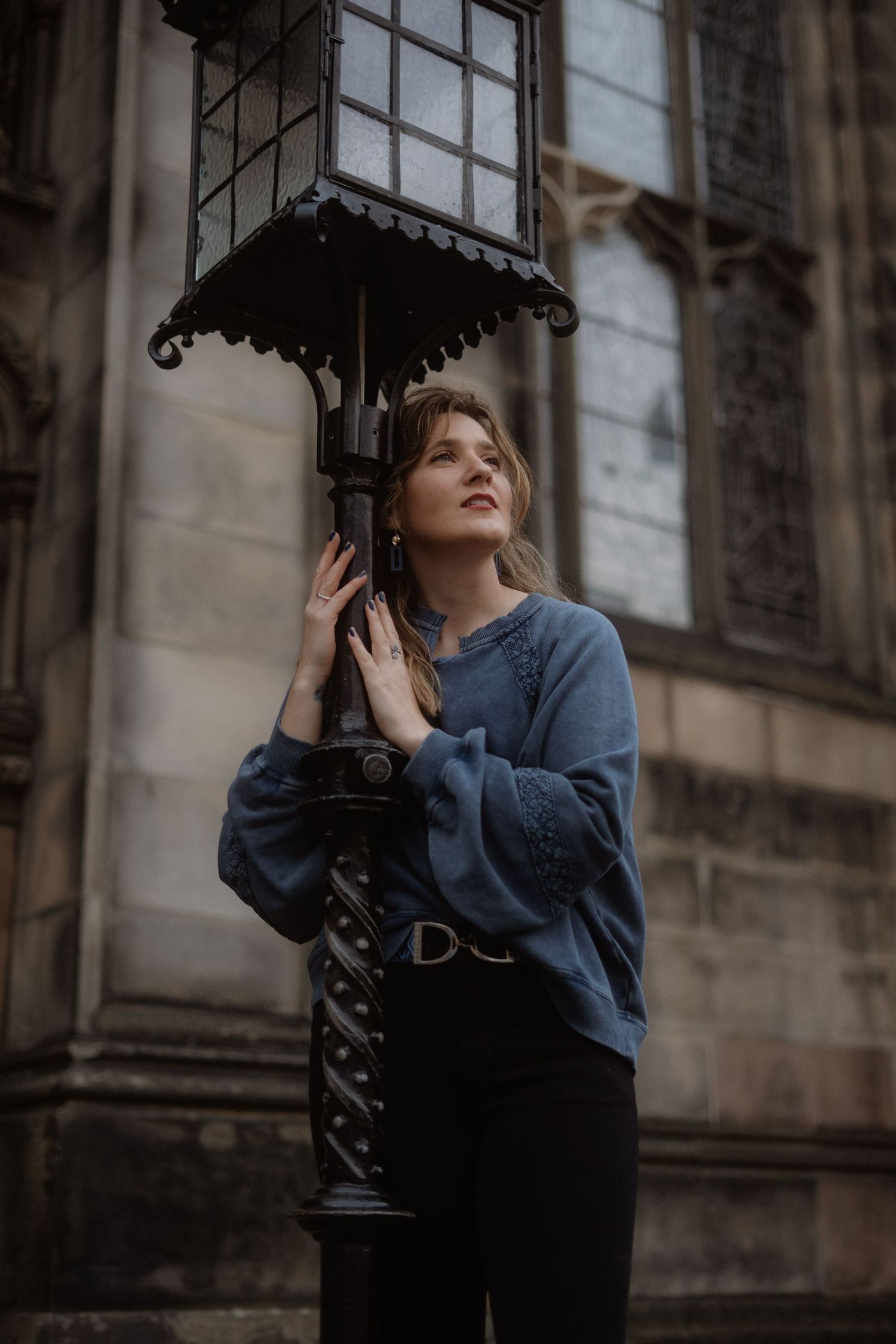 A person in blue clothing poses near an ornate vintage lamp post.
