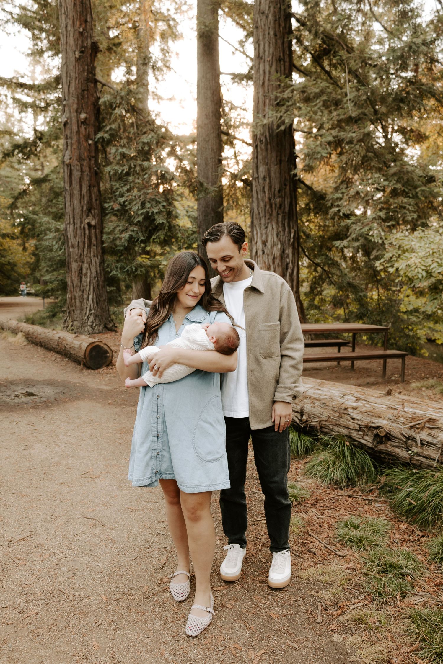 Young couple standing in redwood forest lovingly holding their newborn baby.