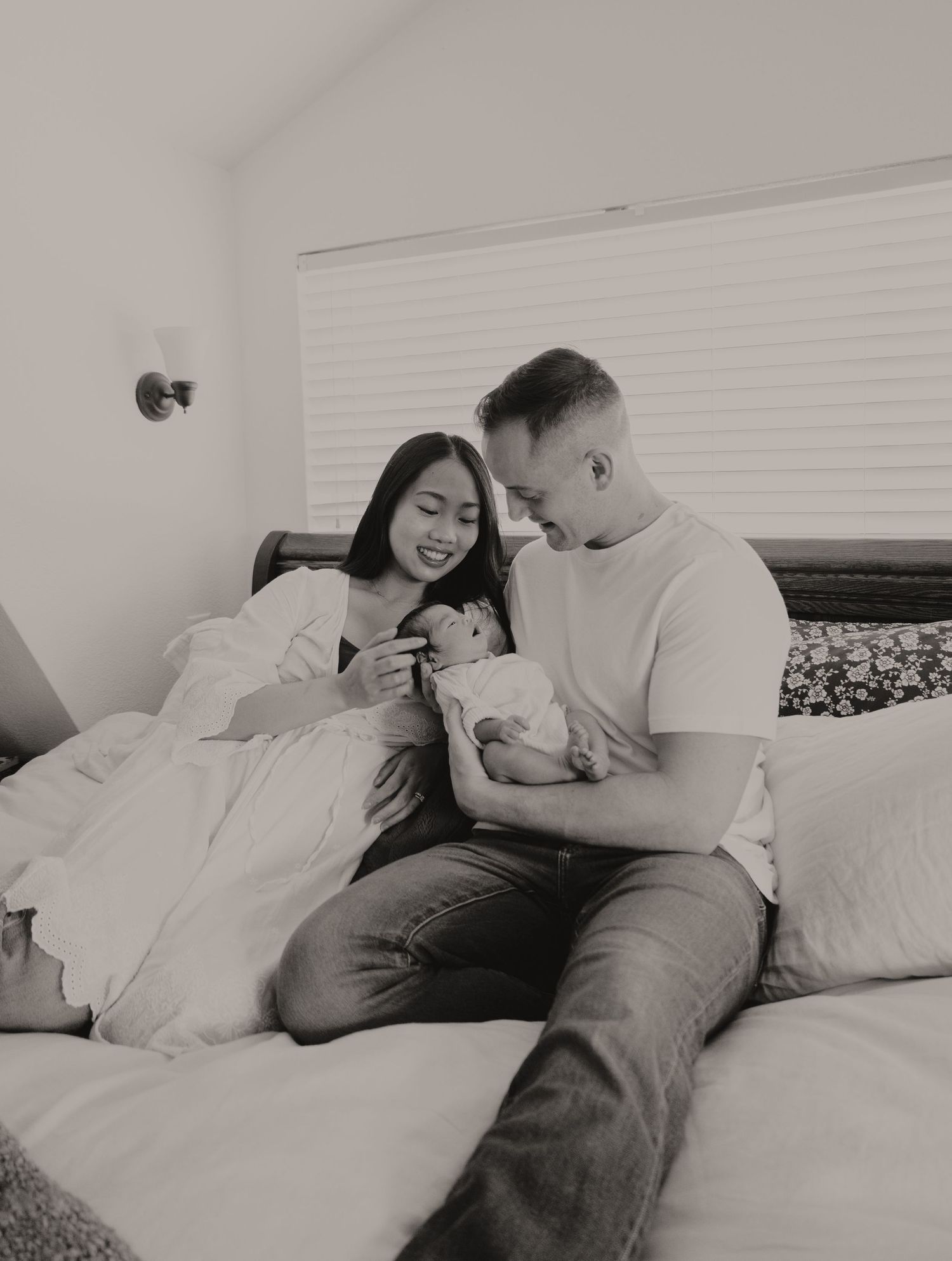Black and white photo of happy parents sitting on bed admiring their newborn baby at home.