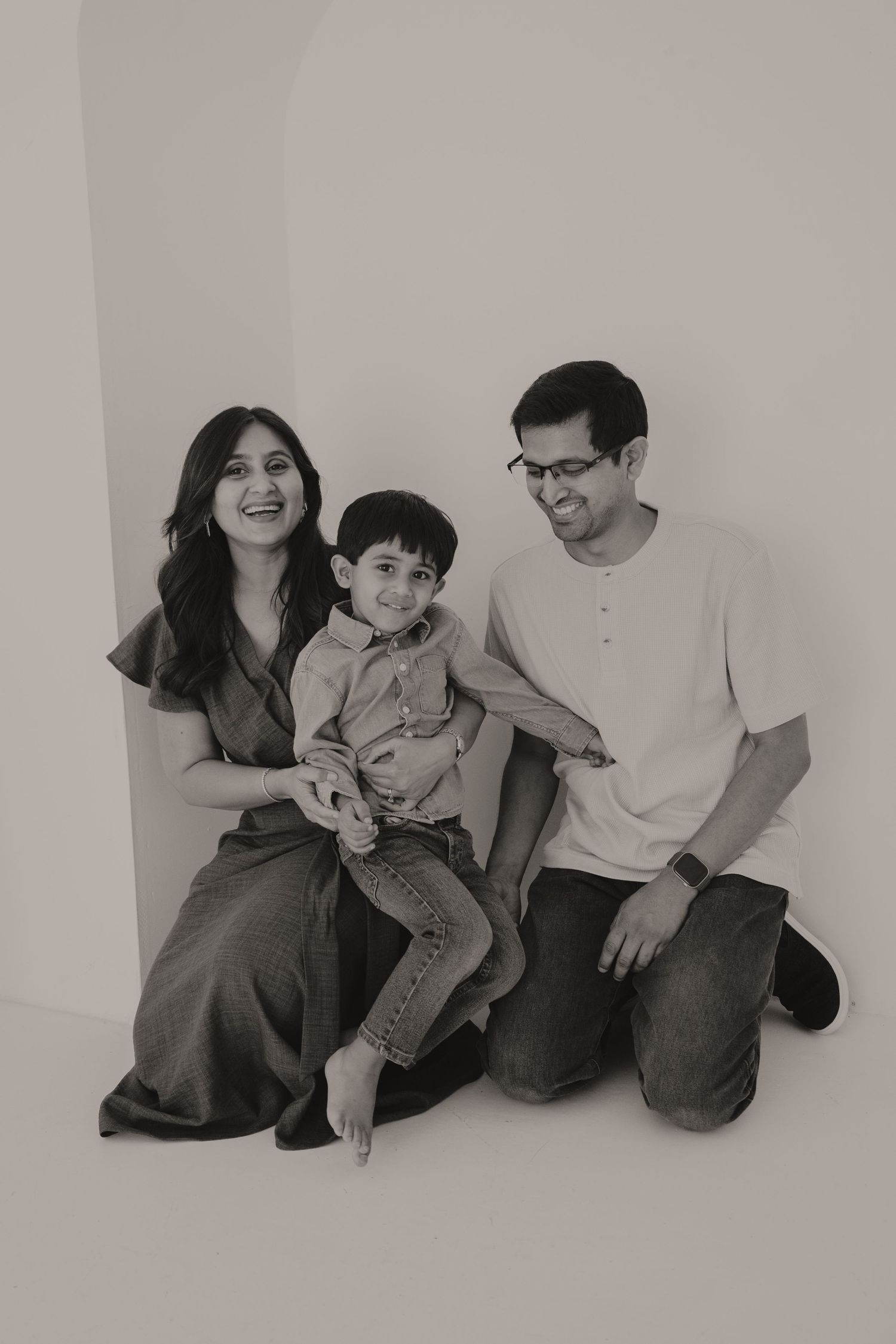 Black and white family portrait of parents and young son sitting together, laughing joyfully.